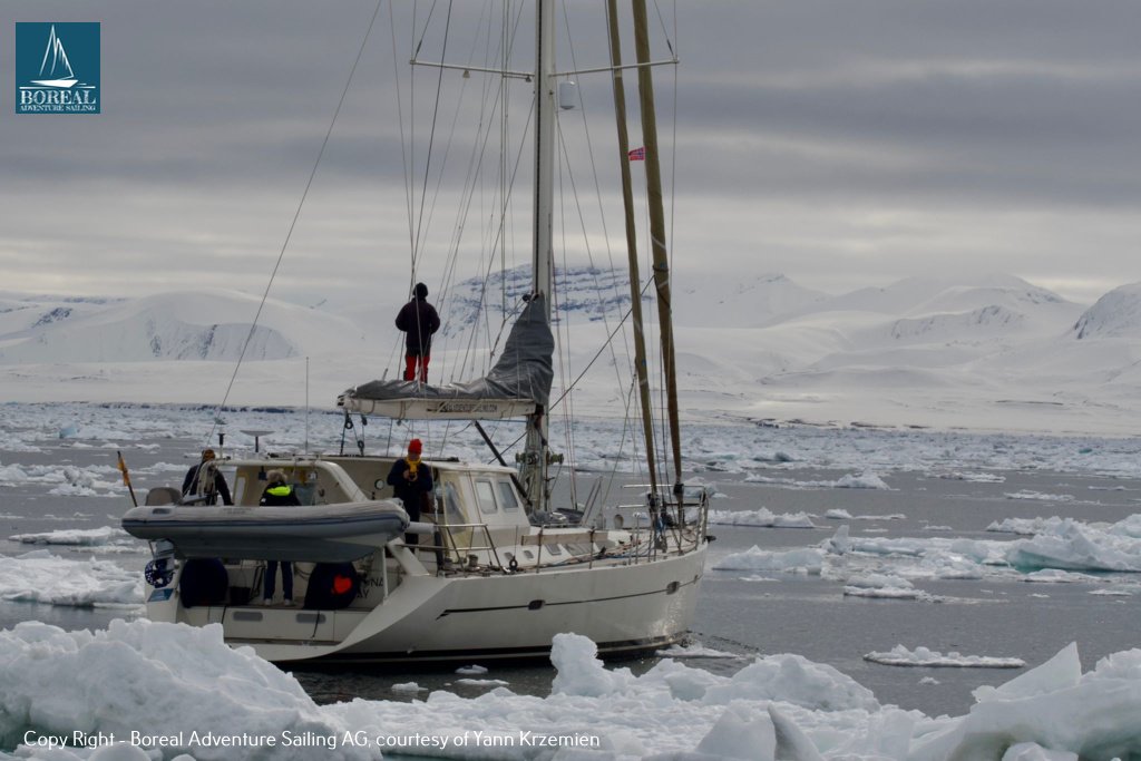 Ski & Sail, Svalbard: yacht with crew on deck among floating ice under a grey sky