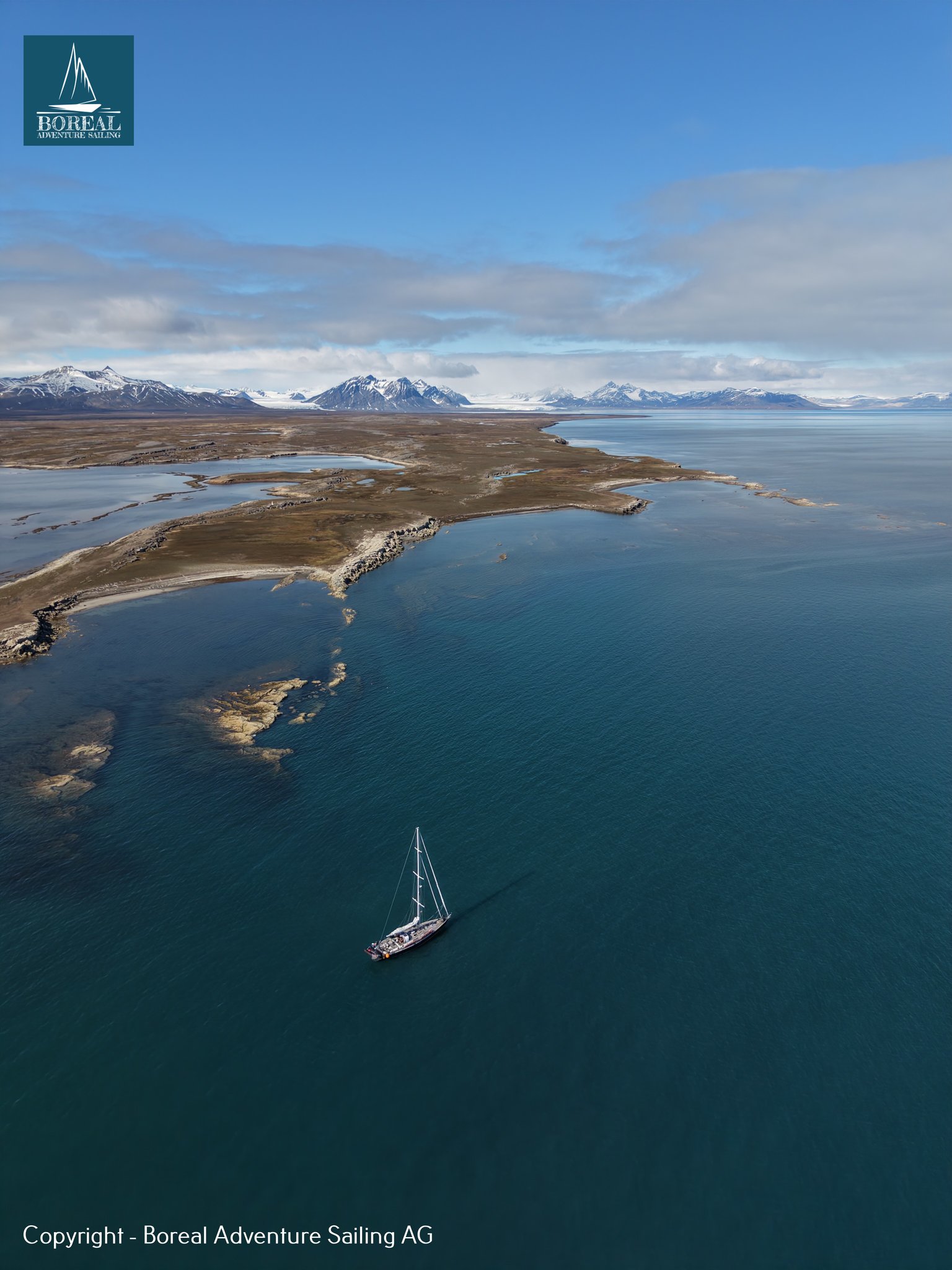 Sail & Explore, Svalbard: aerial view of the yacht in a deep-blue bay beside the tundra