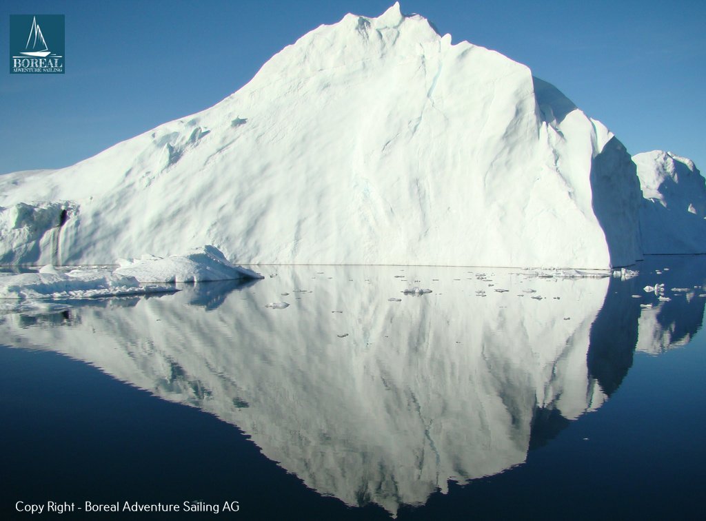 Sail & Explore, East Greenland: towering white iceberg reflected in calm dark water