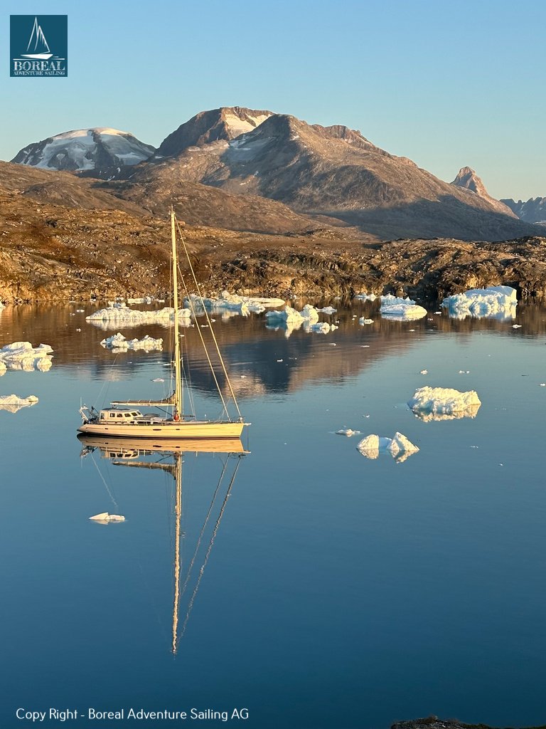 Sail & Explore, East Greenland: yacht anchored among small icebergs beneath mountains in evening light