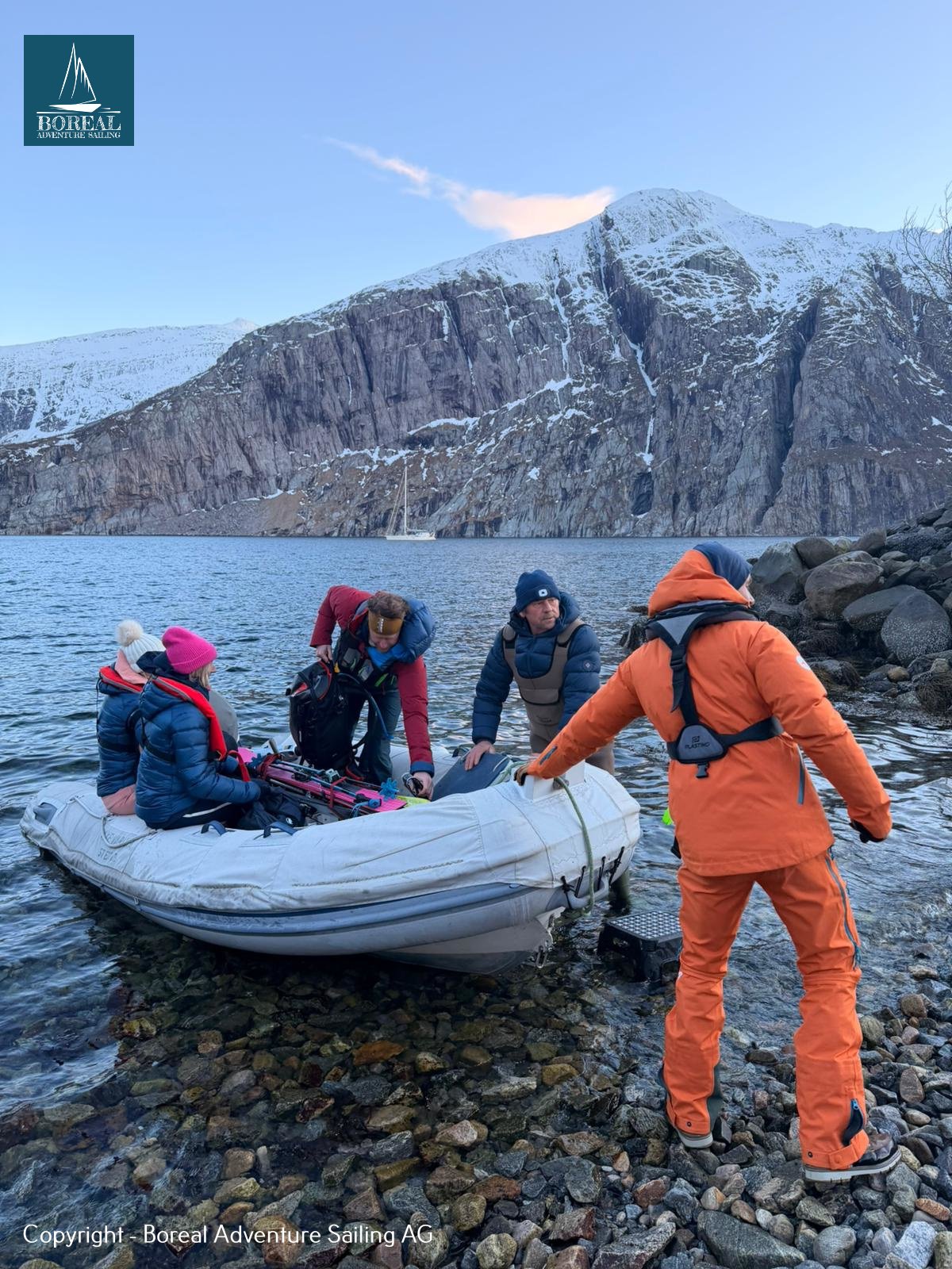 Ski & Sail, Bodø & Lofoten: guests landing by dinghy on a pebble beach below snowy cliffs