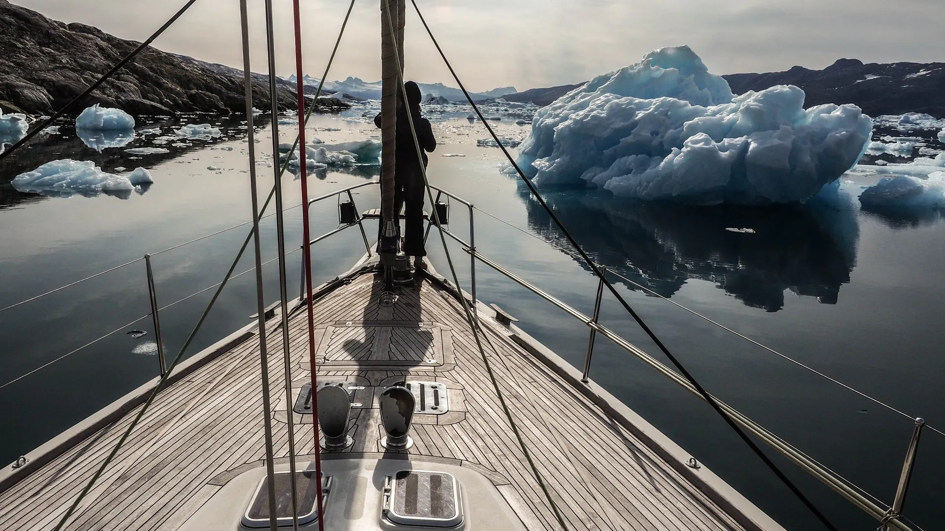 Voile & Exploration, Groenland de l’Est : l’étrave du voilier glissant entre les icebergs dans un fjord calme