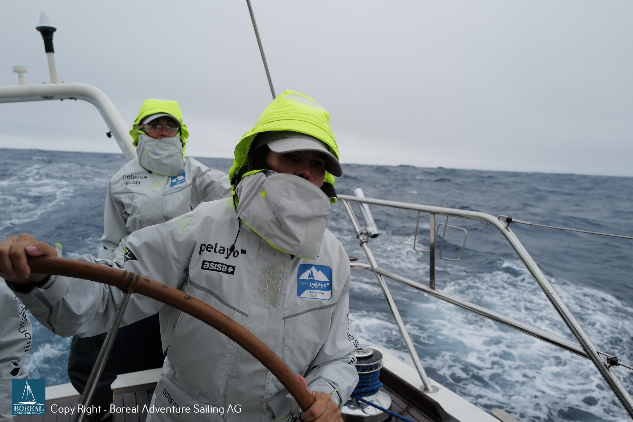 Offshore Sailing: crew in hi-vis hoods at the helm in rough, spray-filled seas