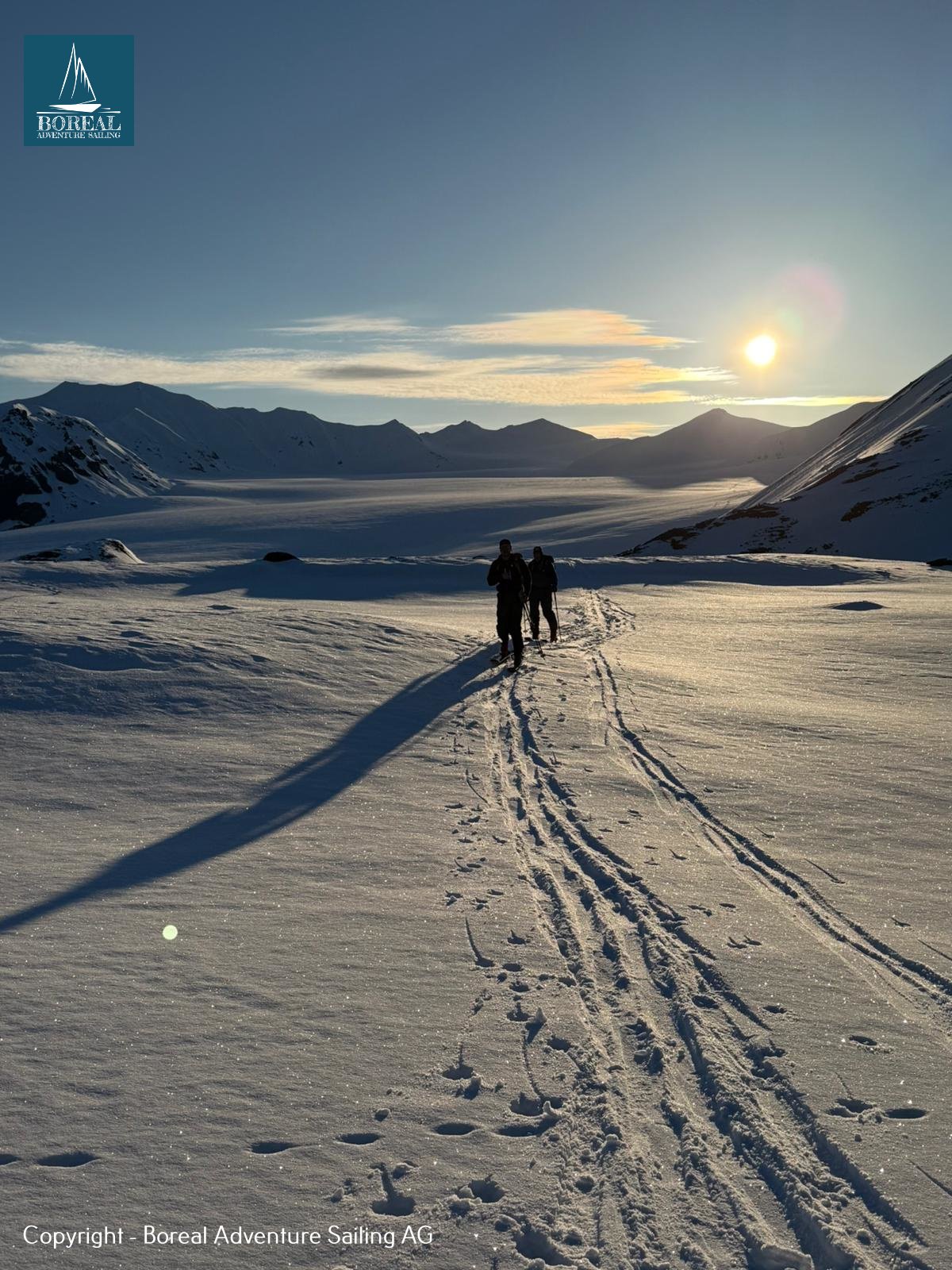Ski & Sail, Svalbard: two ski tourers walking into the low midnight sun