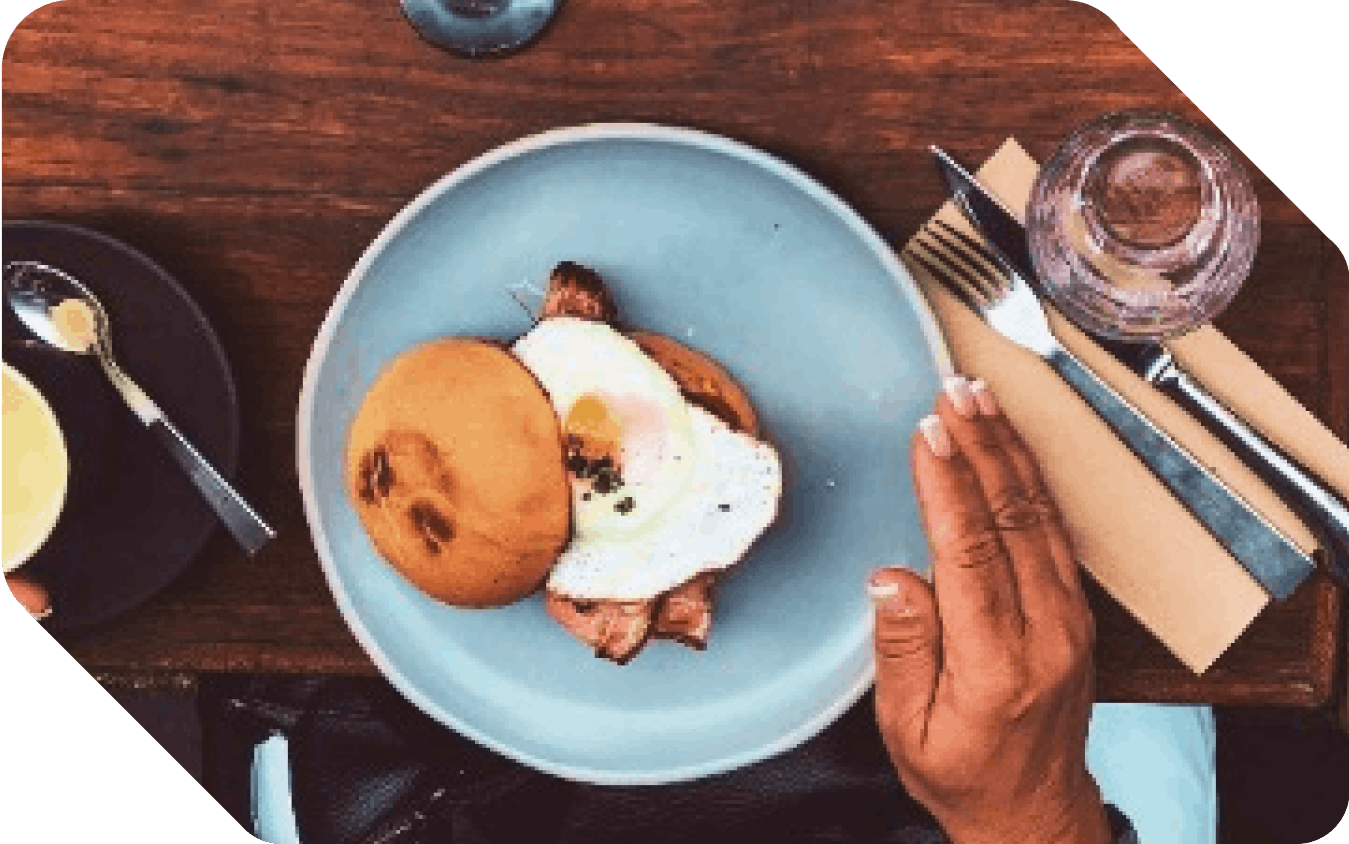 Lightblue plate on wooden table with bun filled sunny side up and fried bacon