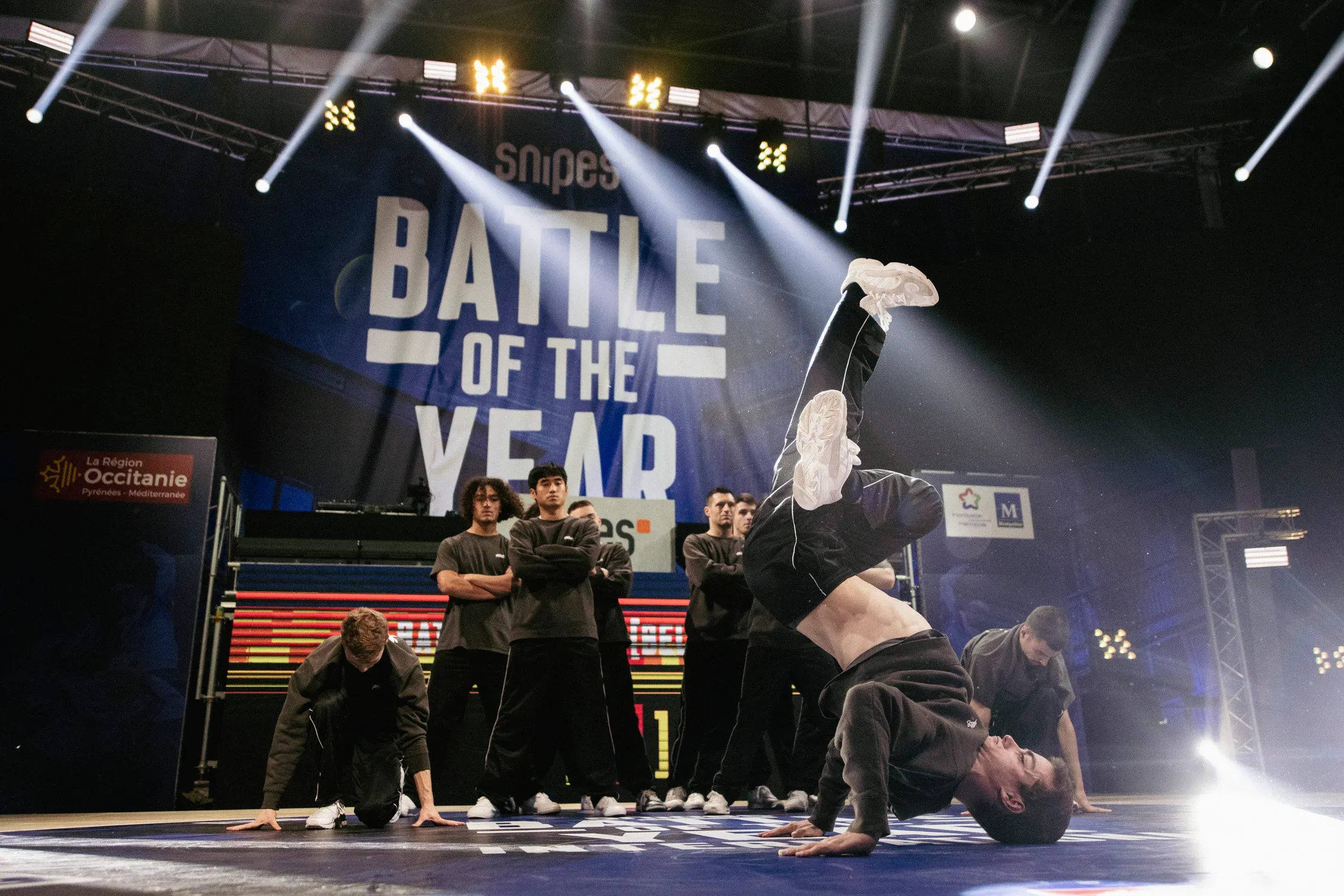 Freeze inversé hero shot avec backdrop BOTY plein cadre, crew en formation