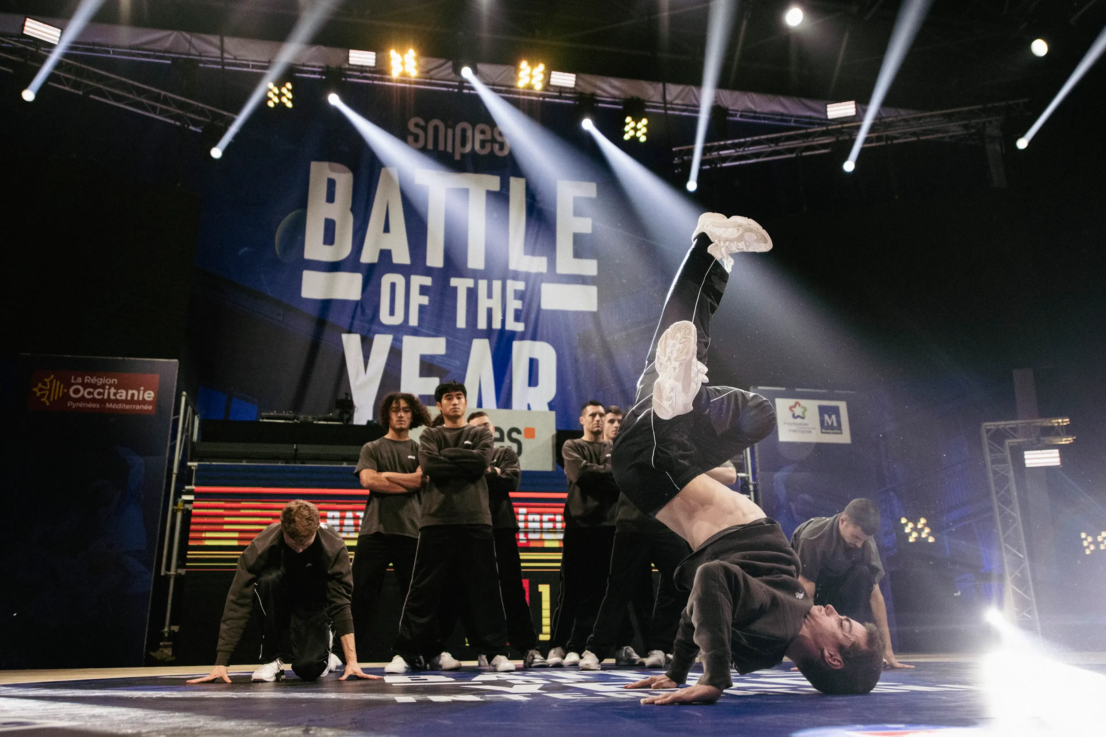 Freeze inversé hero shot avec backdrop BOTY plein cadre, crew en formation