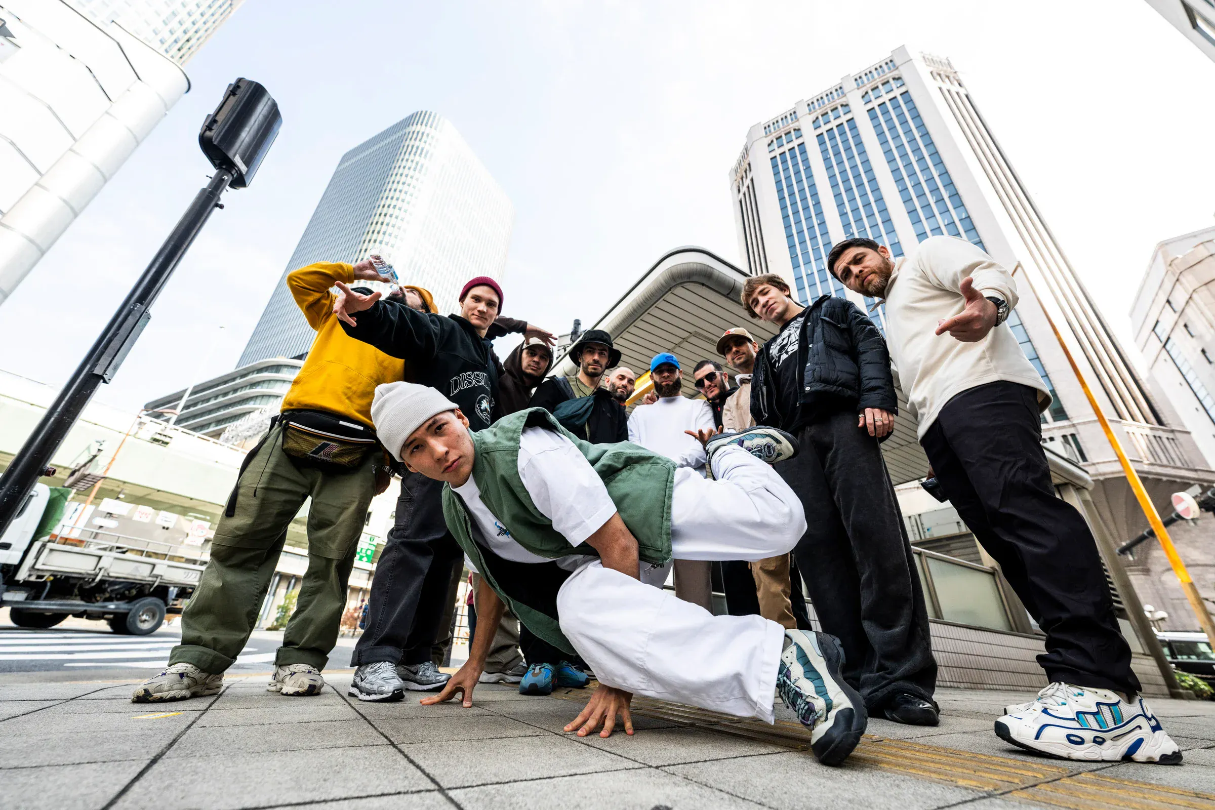 Crew posé wide-angle, freeze central, skyline Osaka — image iconique