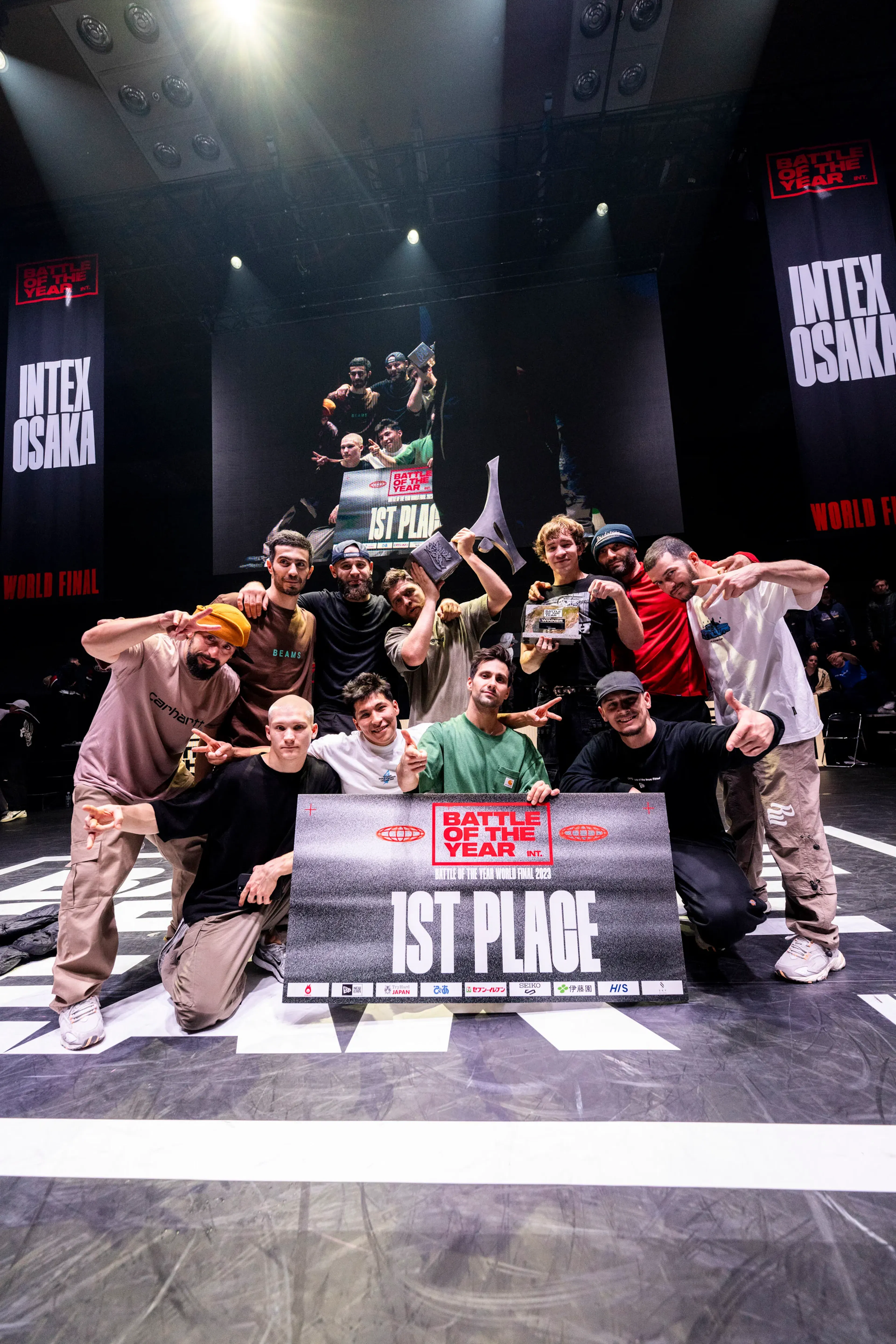 Crew gagnant 1ST PLACE devant écran INTEX OSAKA spotlight, composition forte