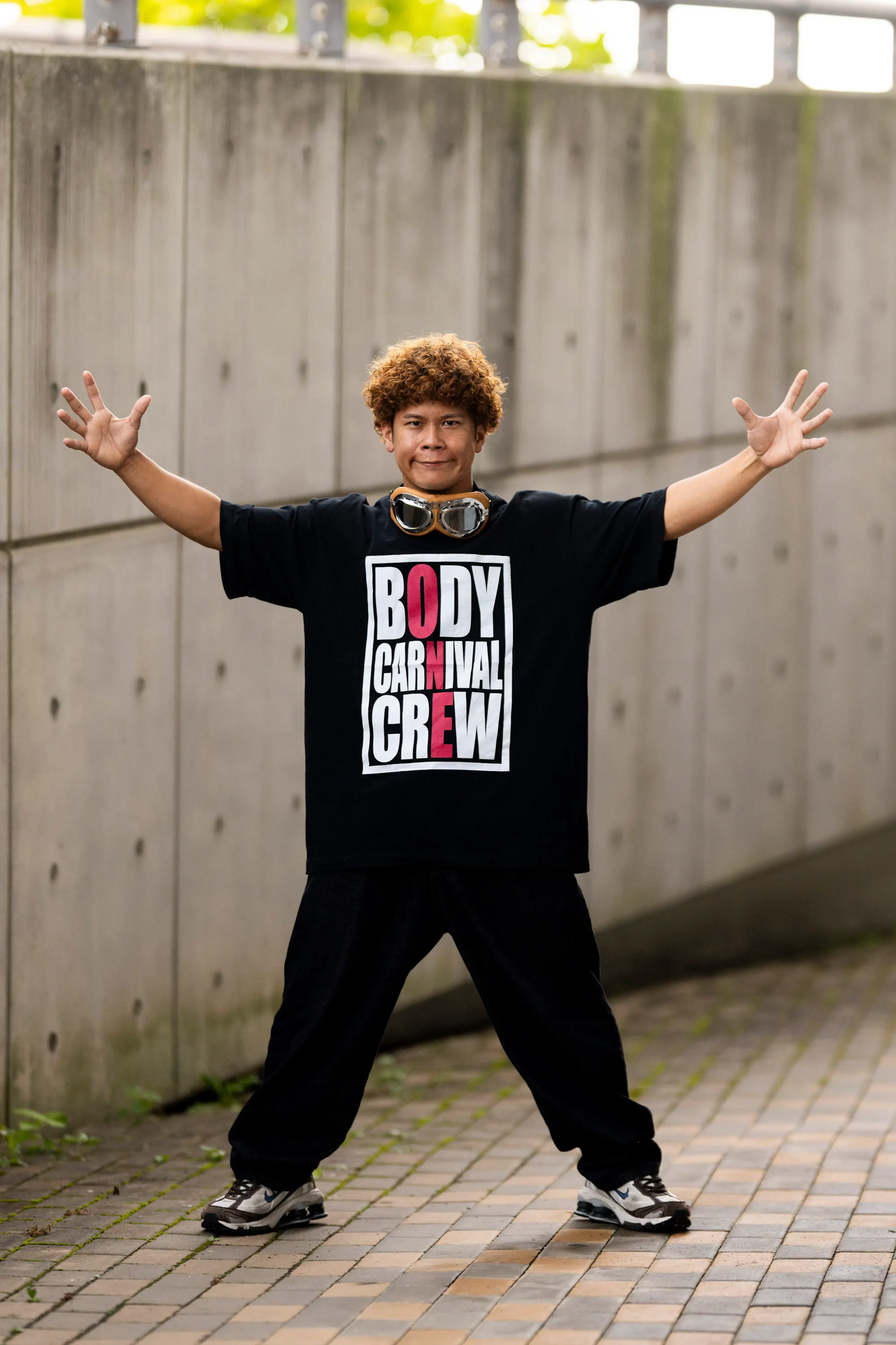 Membre Body Carnival Crew tee logo, lunettes vintage front, bras grand ouverts, sourire généreux