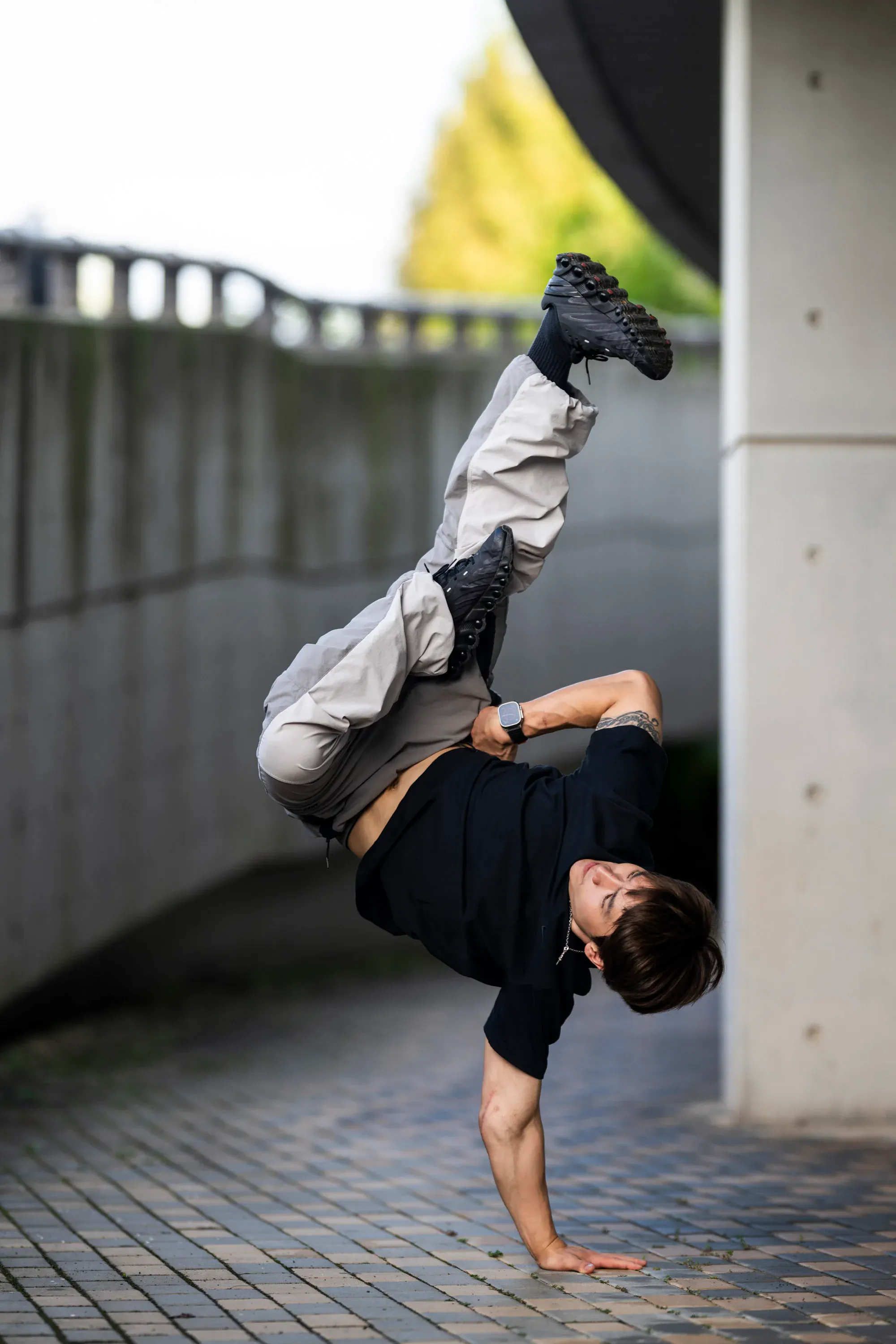 Freeze une-main spectaculaire jambes en l'air sous coursive béton, pavés au sol, dynamique très forte
