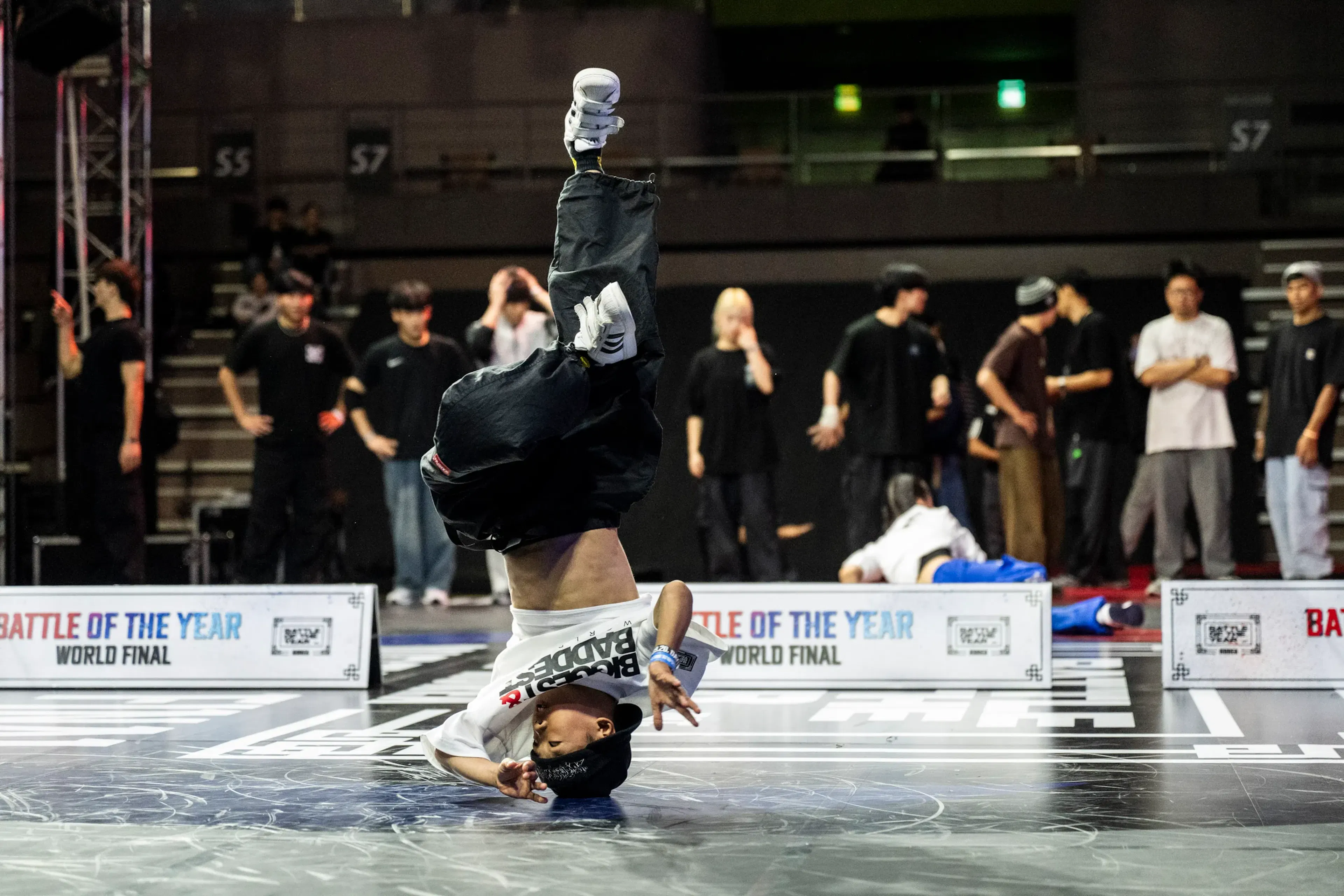 Freeze tête en bas pieds vers le ciel, t-shirt blanc 'BBOY BADDER', bandeau 'BATTLE OF THE YEAR' net derrière