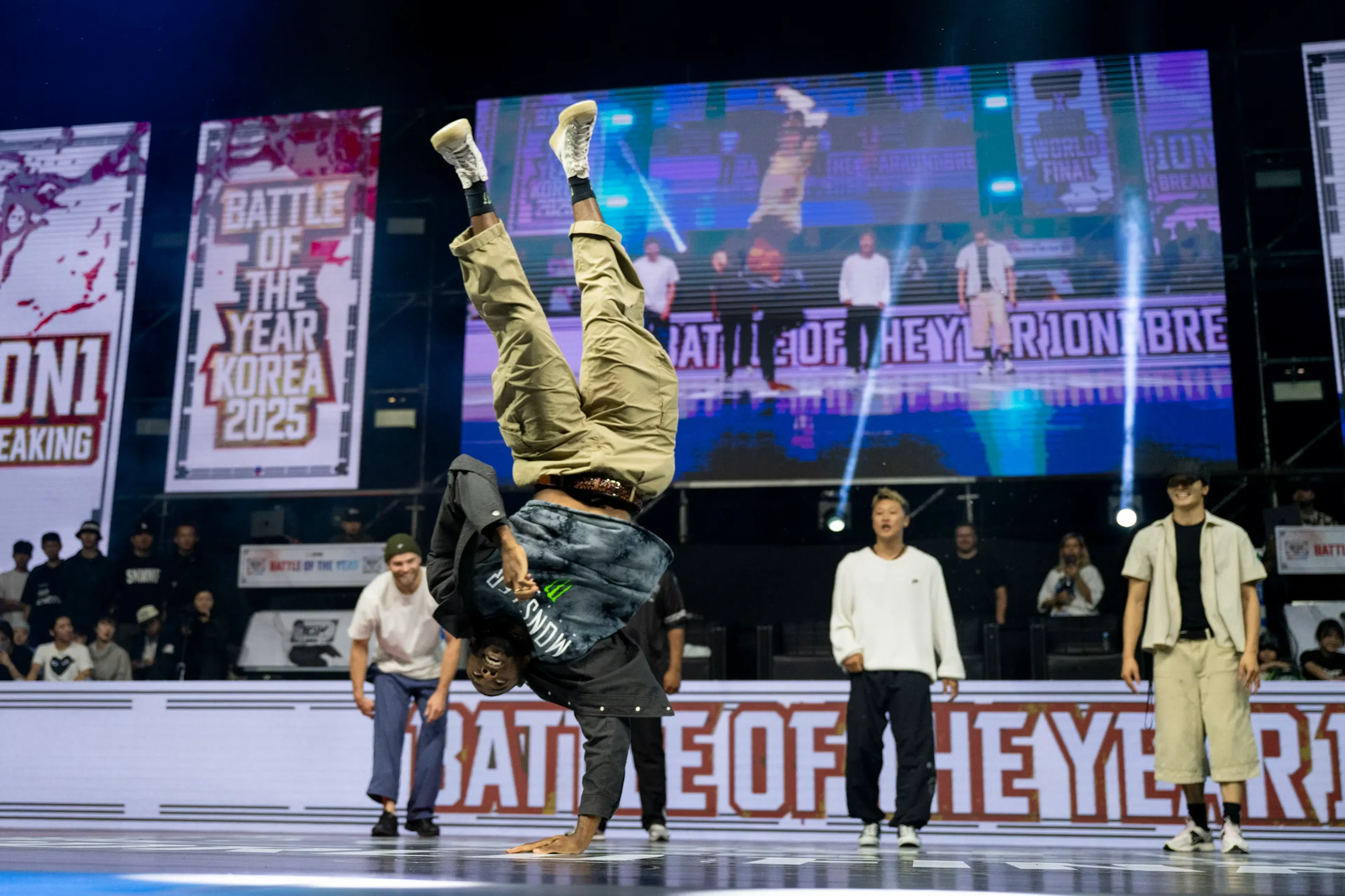 Bboy en handstand parfait jambes verticales pantalon camo, écran BATTLE OF THE YEAR derrière