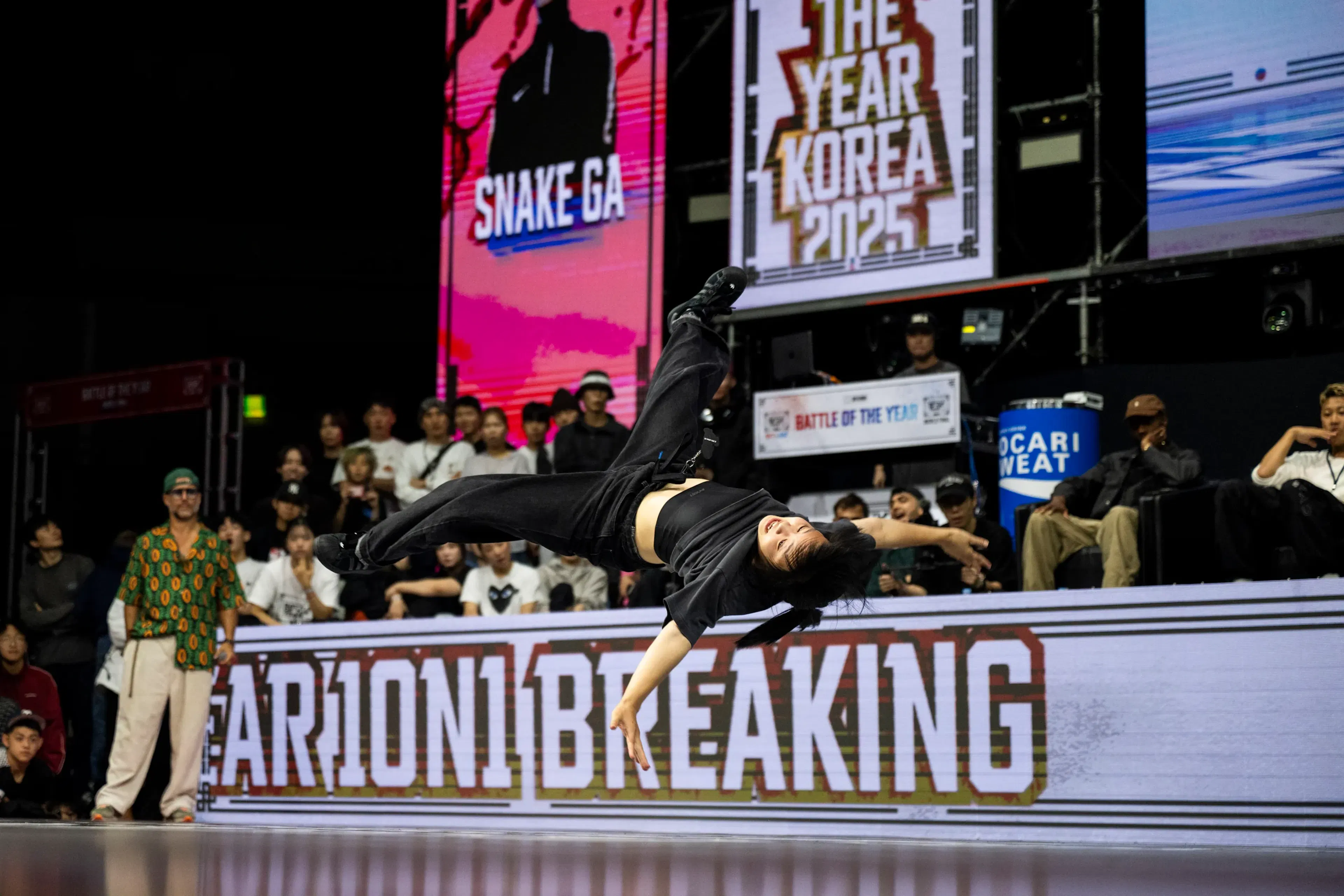 Bgirl en flag horizontal complet bras tendu, écrans SNAKE GA rose et KOREA 2025