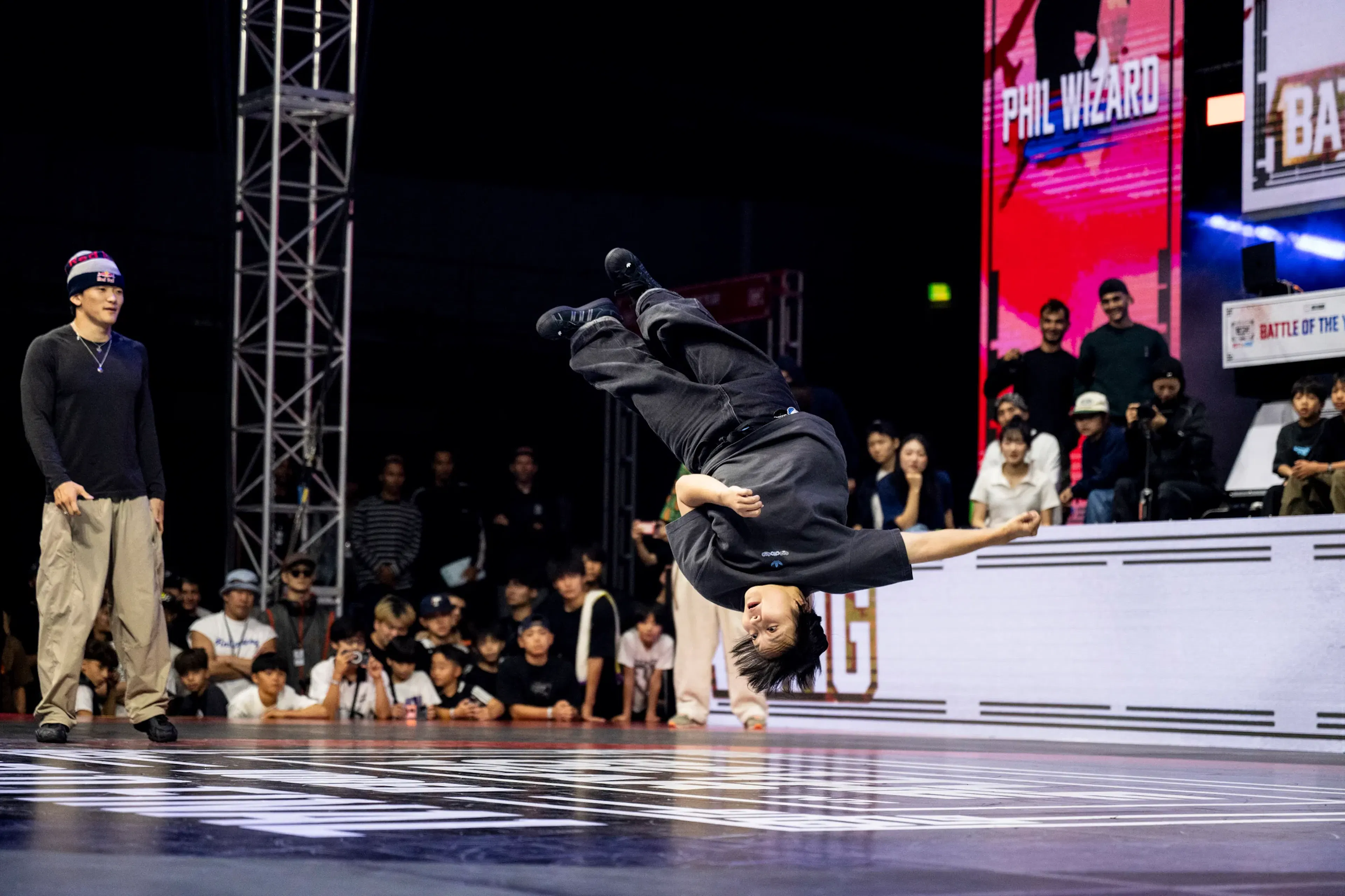 Phil Wizard suspendu en plein flip aérien, jambes en l'air, écran rouge avec son nom — image emblématique