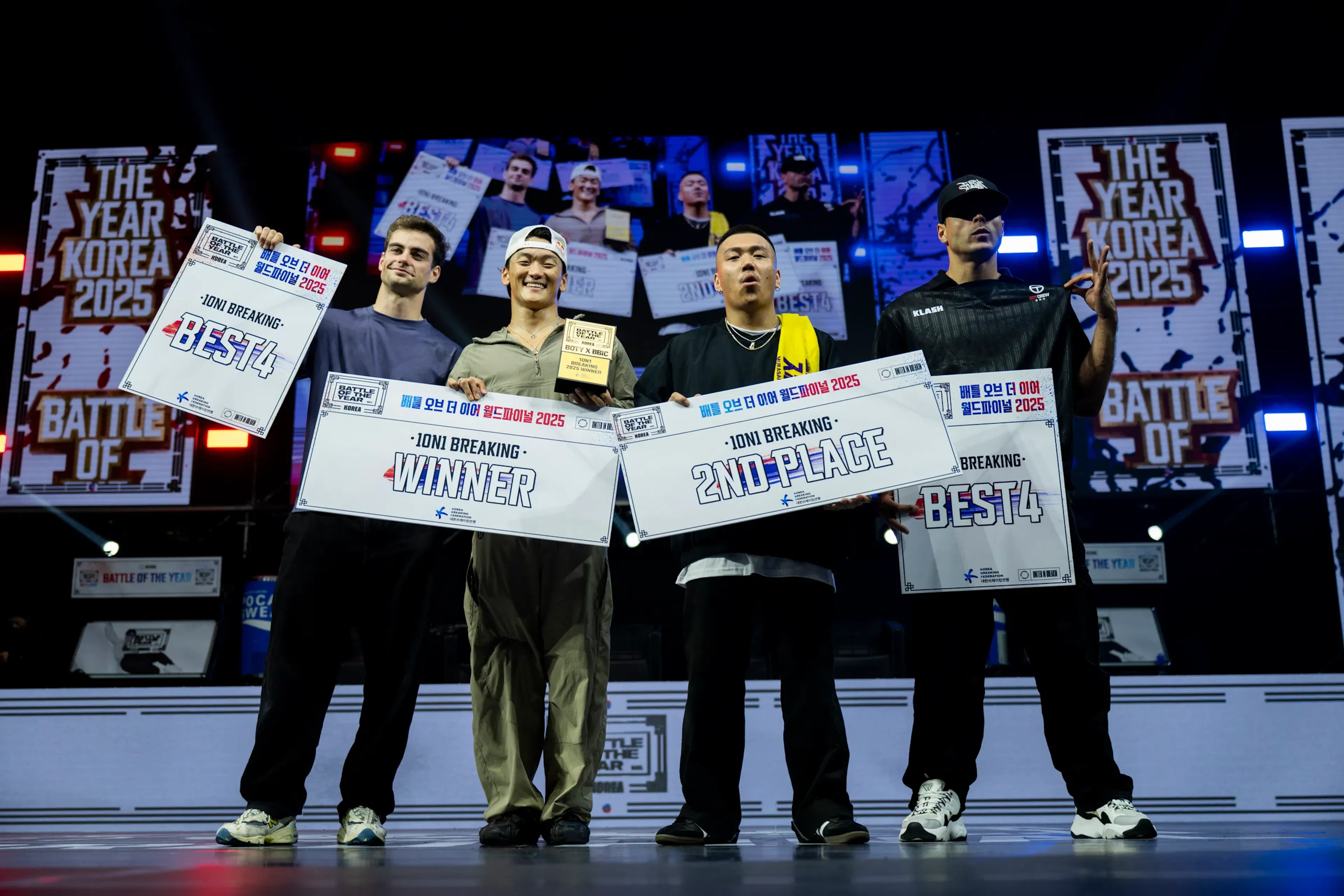 Podium 1on1 complet 4 finalistes alignés avec pancartes Winner/2nd/Best4, écran Korea 2025