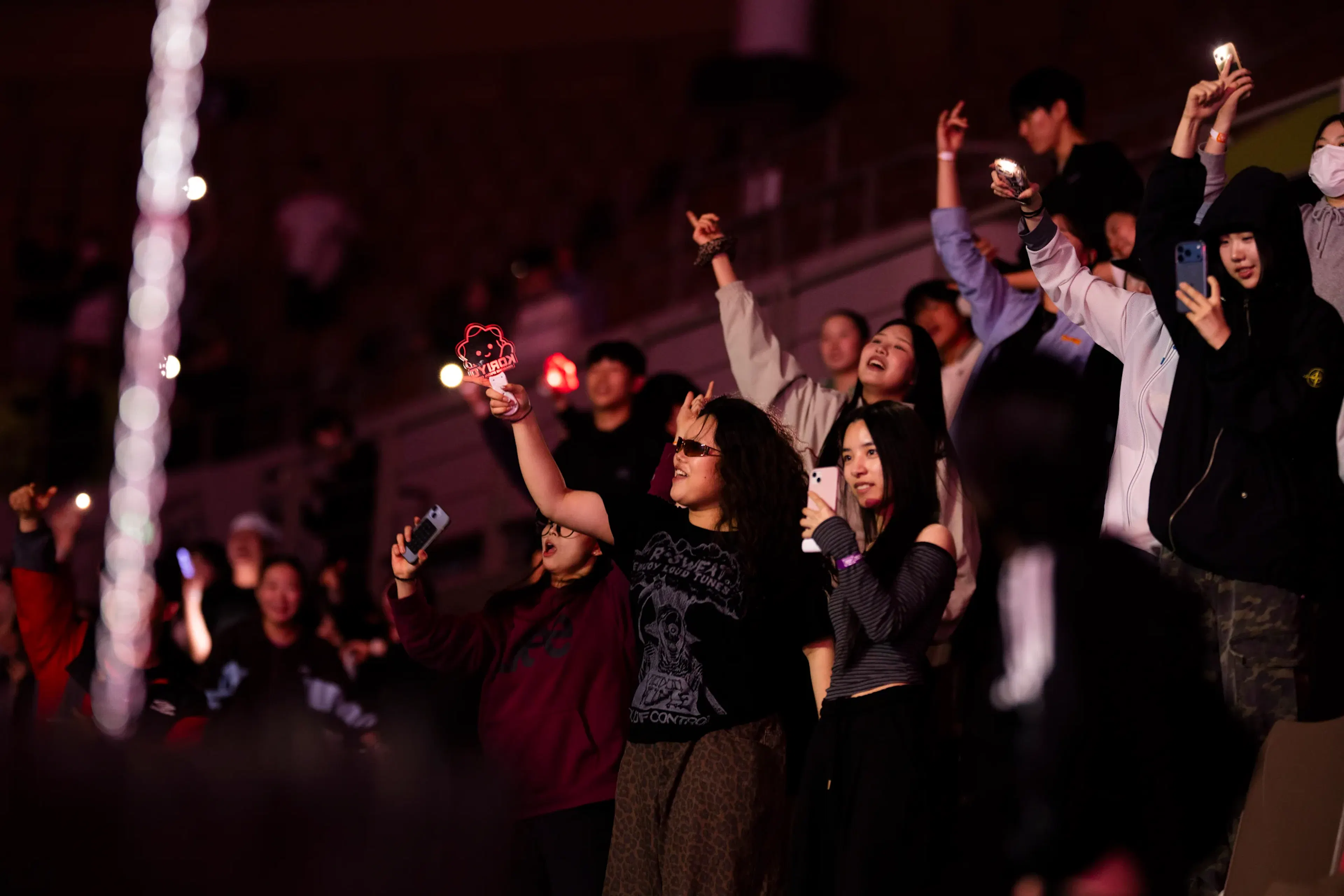 Public féminin debout cheering main levée smartphones, lumière rouge gradins