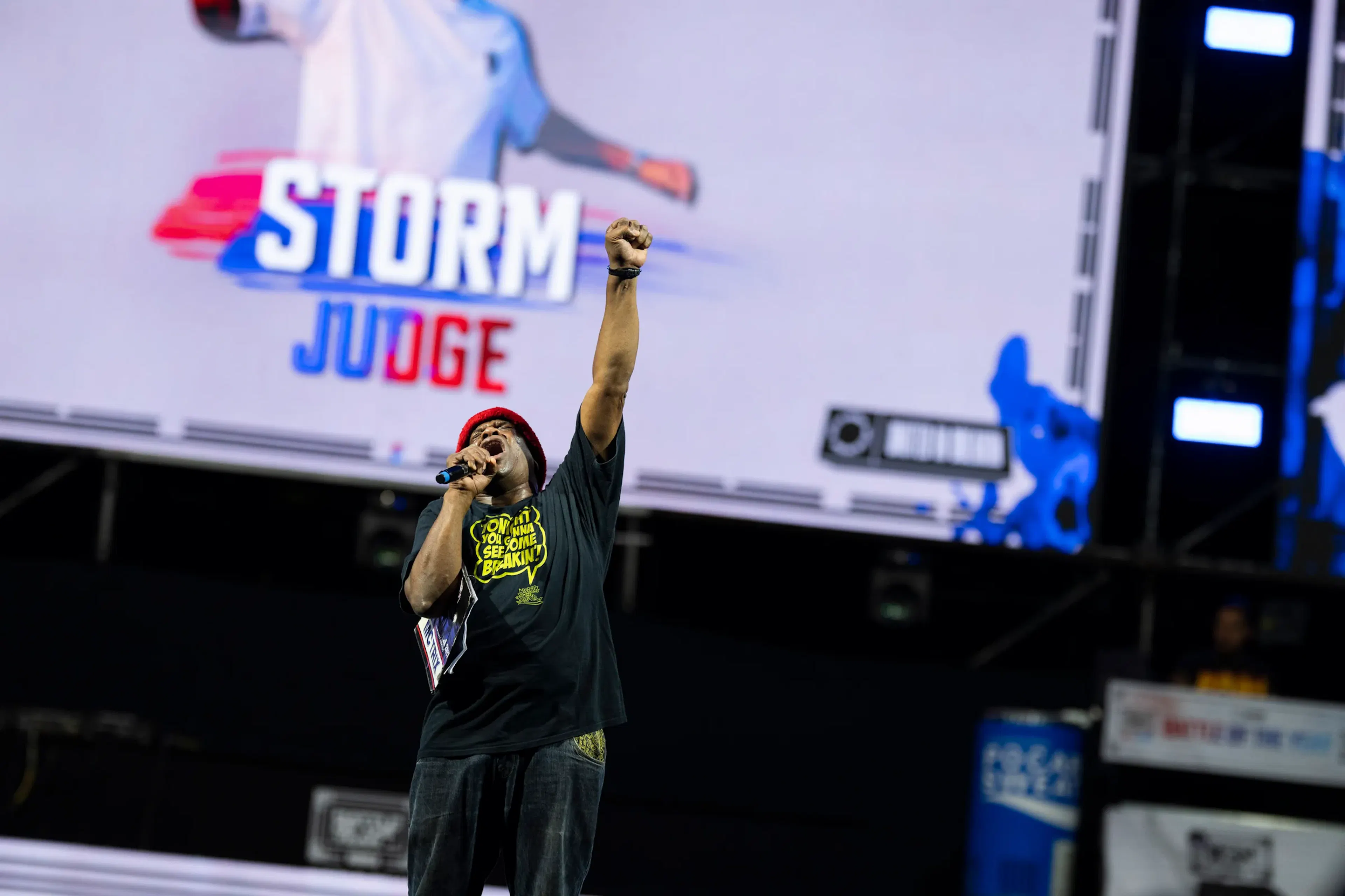 Storm en plein cri poing levé, écran derrière marqué STORM JUDGE, charisme intense