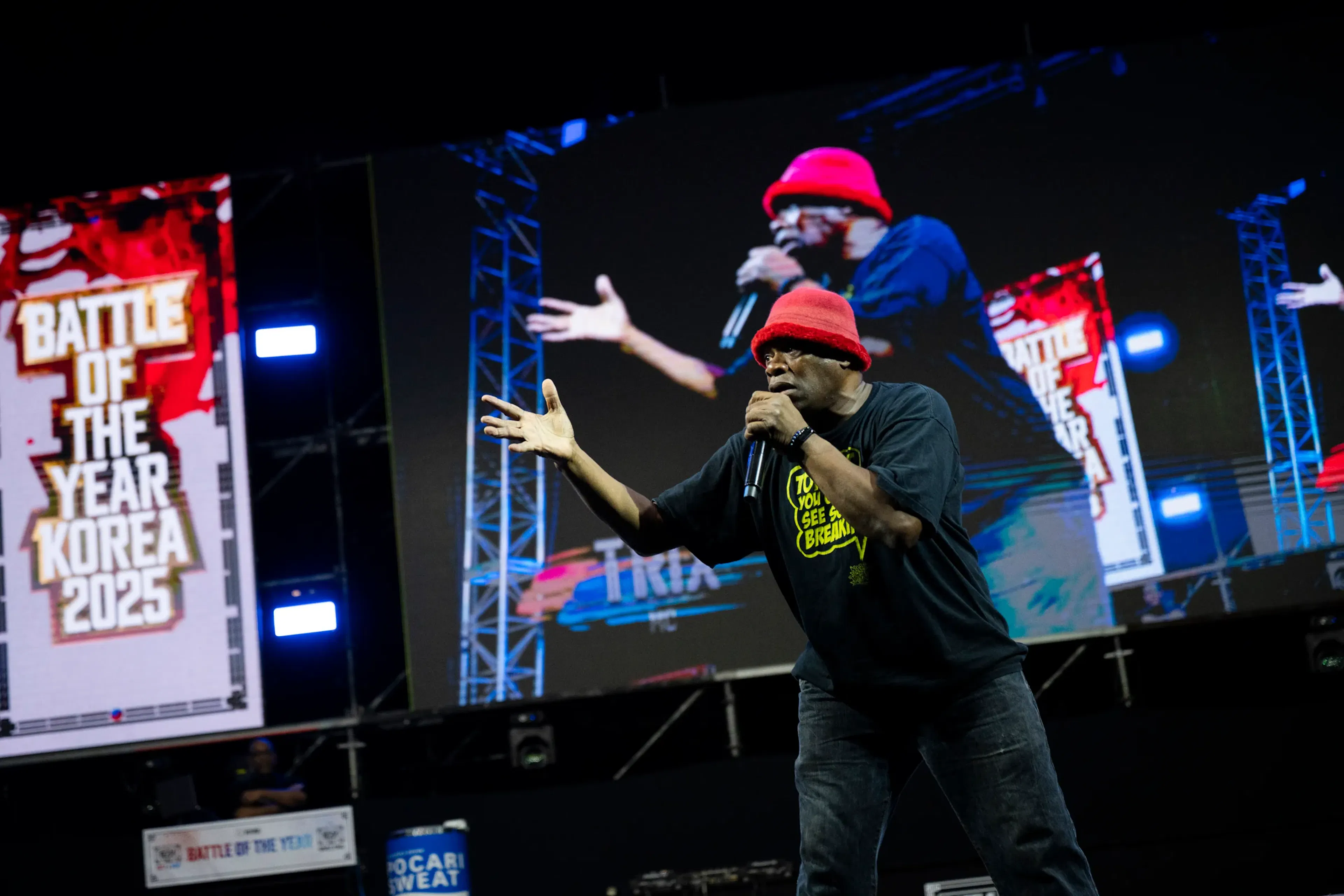 MC bonnet rouge mic main tendue, double exposition écran géant en miroir, énergie vocale