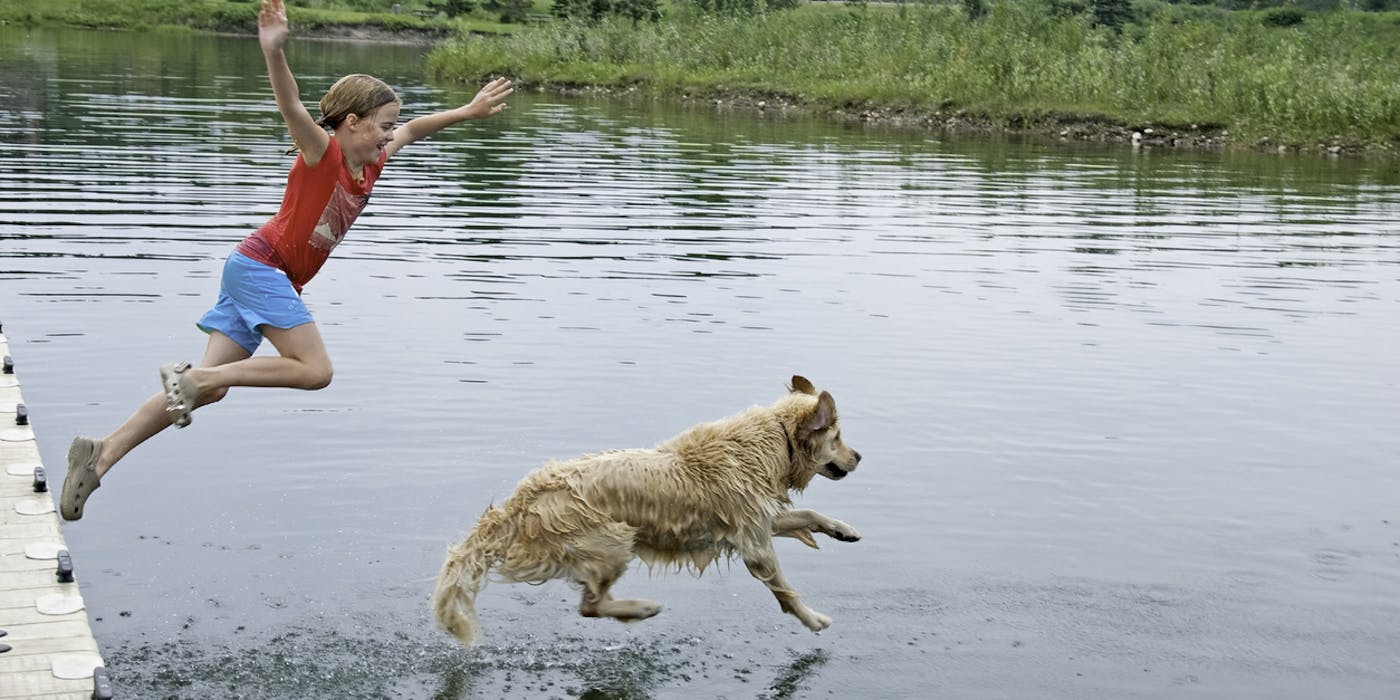 A girl jumping in the water with a dog