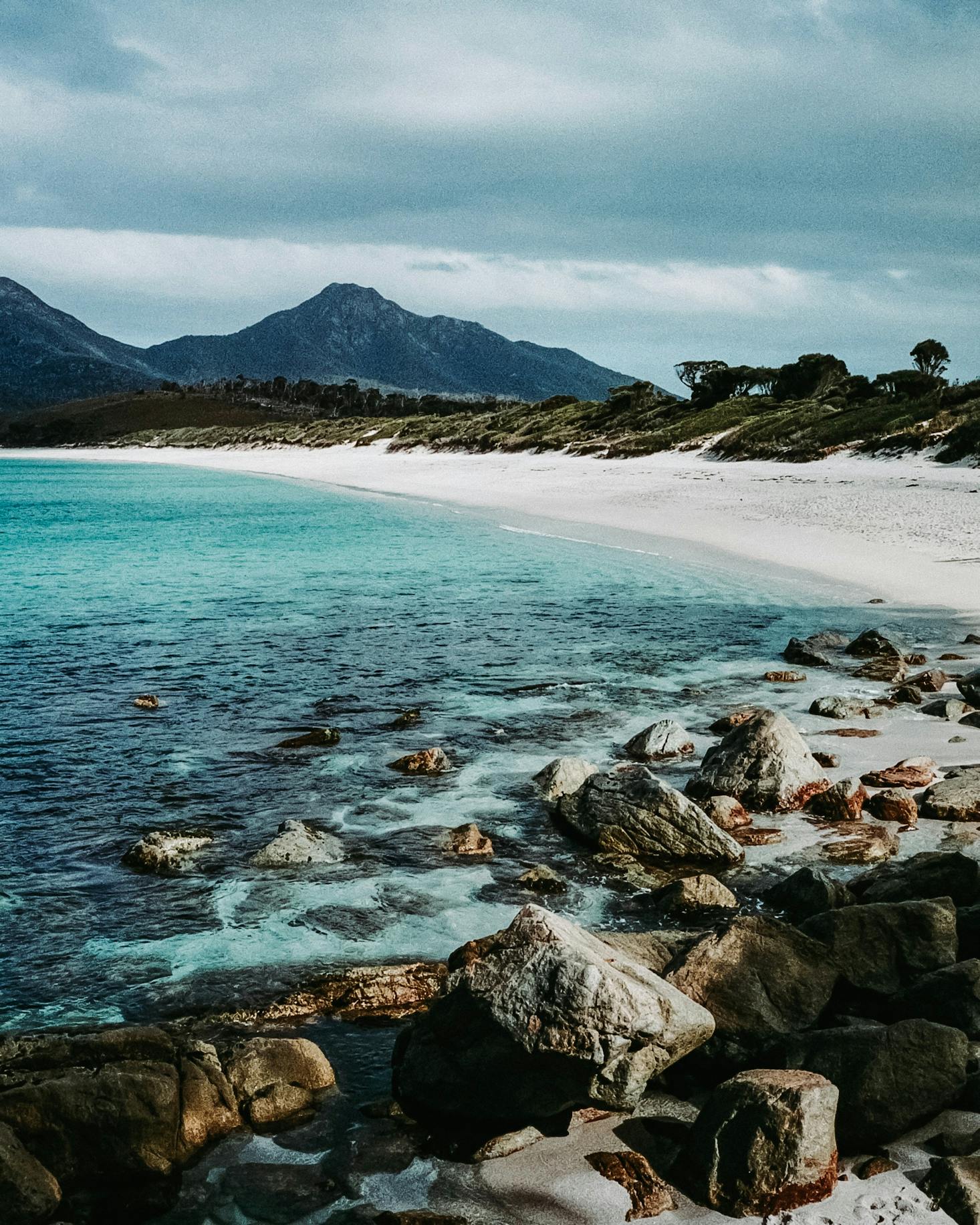 Beach in Hobart with clear blue water, white sand, and mountains 