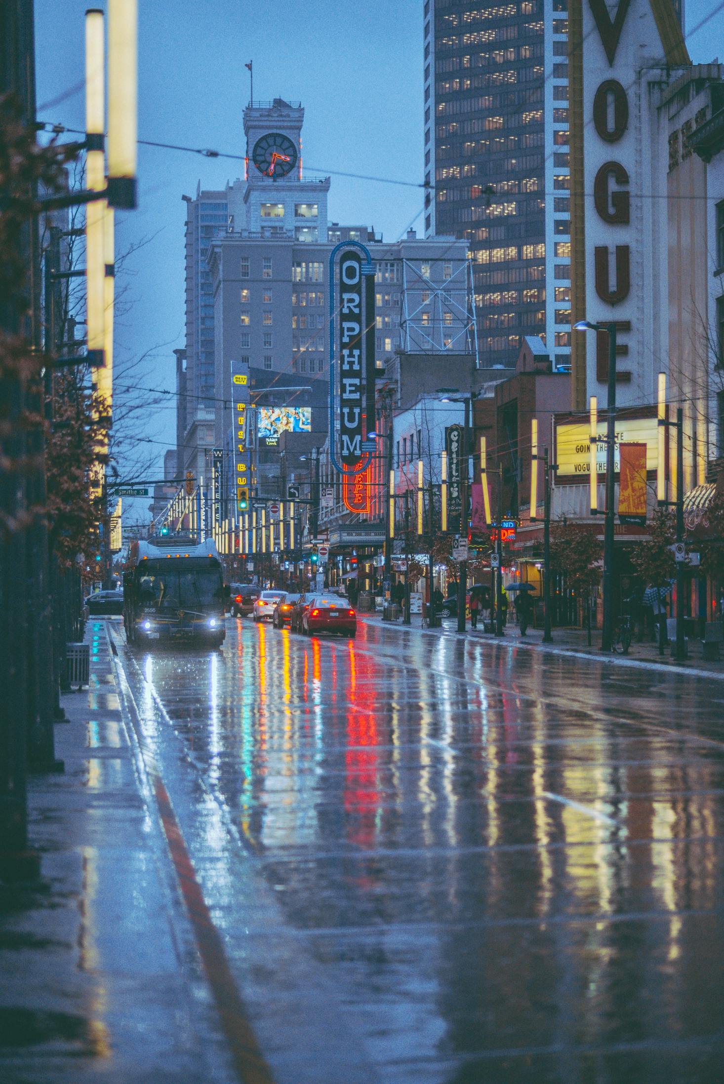 A bus driving on a wet street in Vancouver at dusk