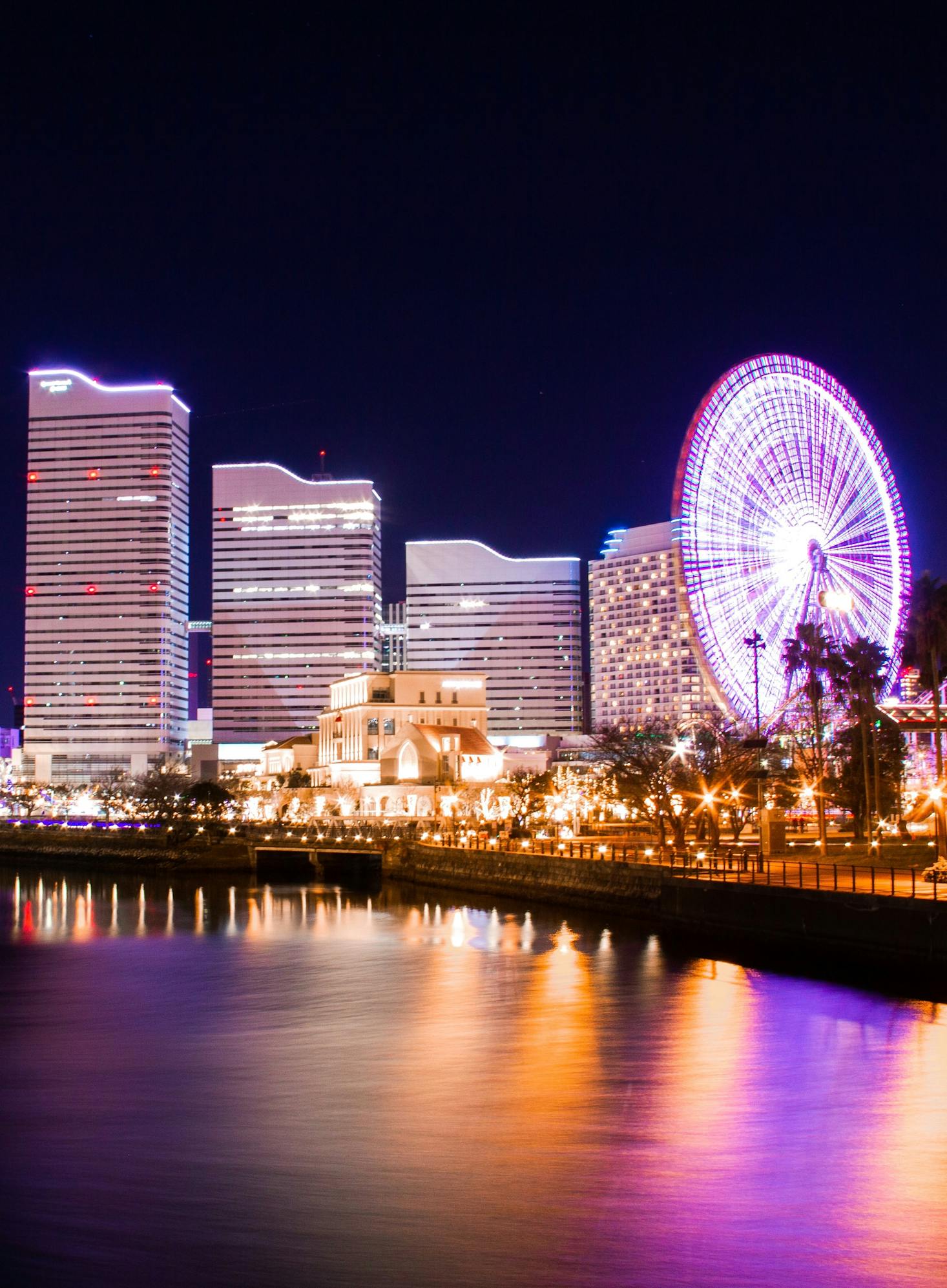 The Yokohama waterfront lit up at night with skyscrapers and a large, white Ferris wheel