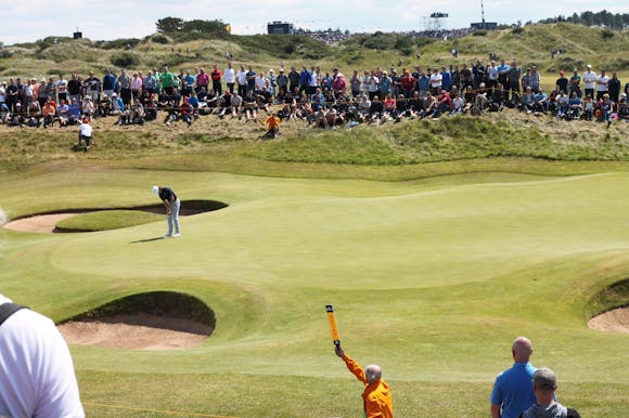 Large crowd seated and standing around a golf course, intently watching a golfer in action at the Waste Management Open