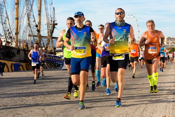 A group of exhausted marathon runners racing down the street next to a port