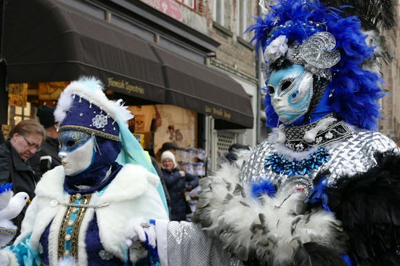 Two participants dressed in blue and white costumes walking in the Viareggio parade, with spectators watching