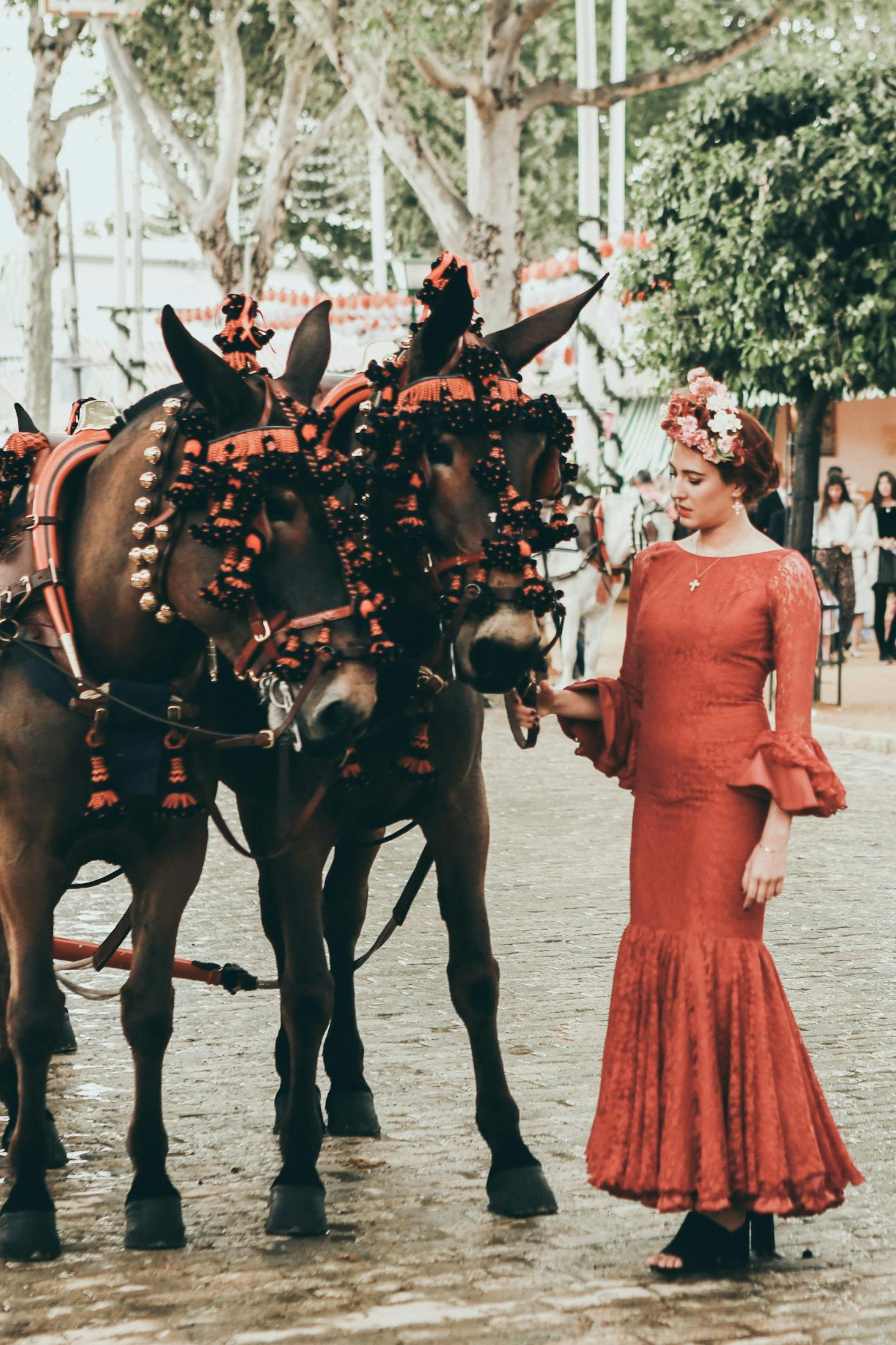 Una donna in abito da flamenco vicino a cavalli decorati per le feste.