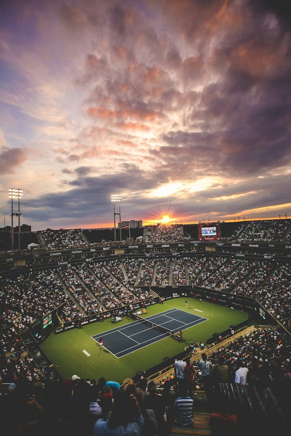 Tennis stadium filled with a large crowd watching a match as the sun sets, capturing the atmosphere of the Indian Wells