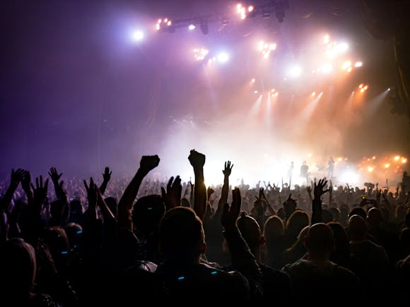 A lively crowd with their hands up in the air listening to performers at a music festival