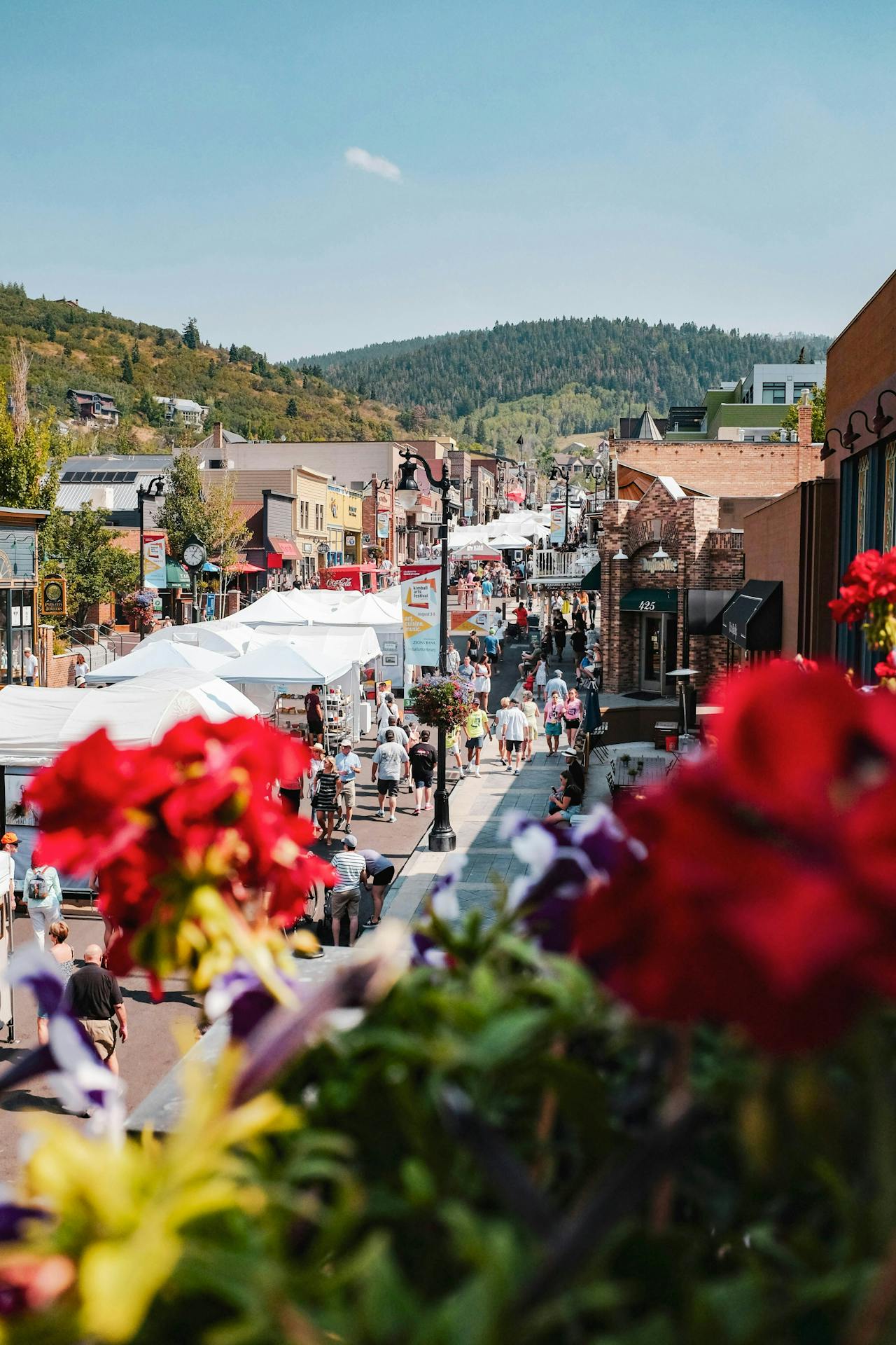 A crowdy and sunny street filled with stalls and art pieces, with green mountains in the background 