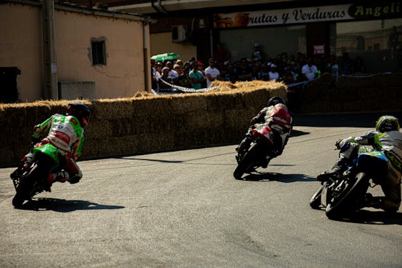 Three MotoGP riders on a sharp turn during a race with spectators watching on the side