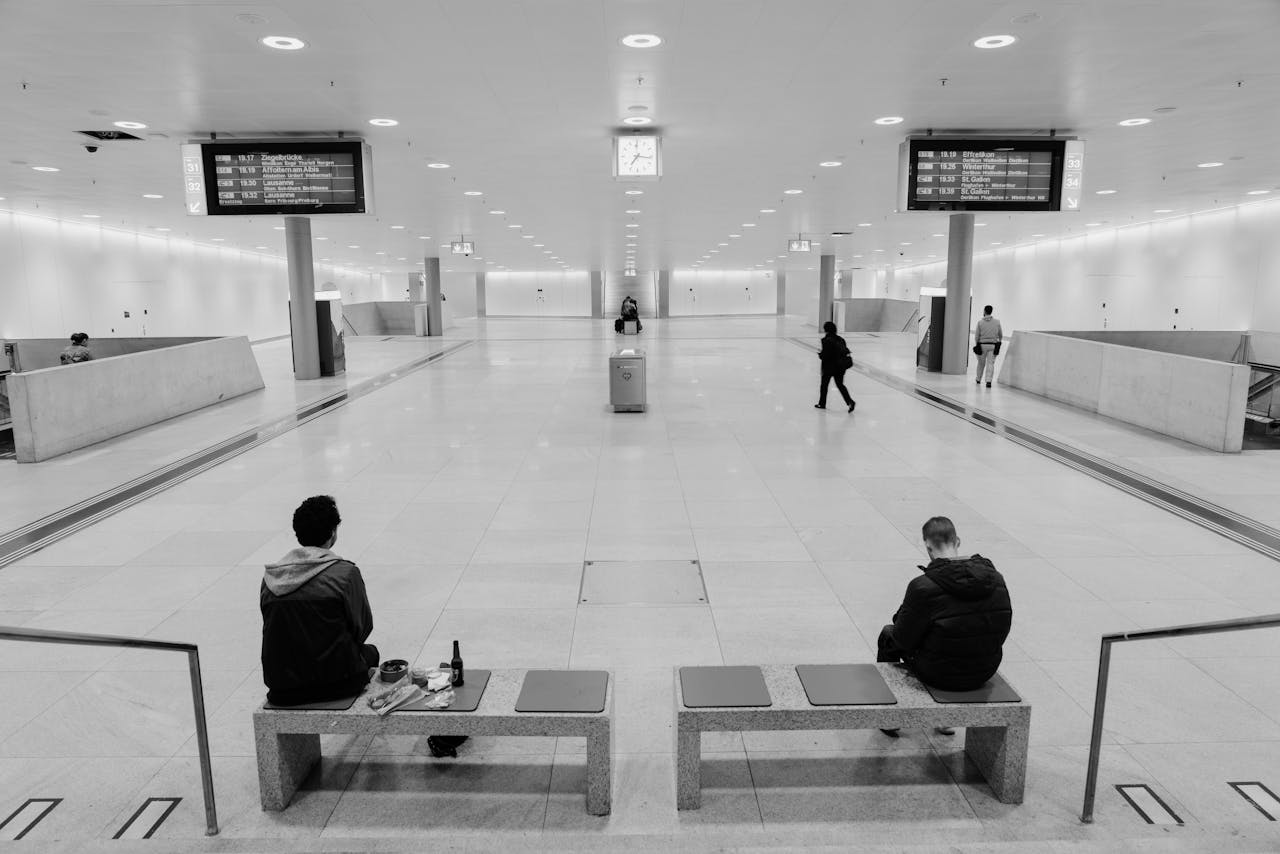 Zwei Männer sitzen auf Bänken in einer ruhigen Empfangshalle, Hauptbahnhof Zürich