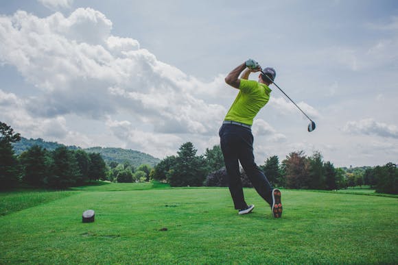 Golfer in a yellow T-shirt hitting the ball on a vast green golf field