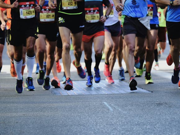 Lower half shot of many runners wearing bibs and running a marathon on a paved road