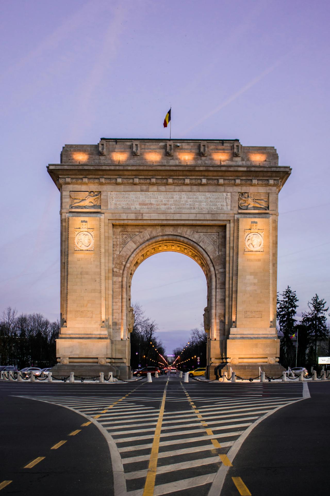 Arcul de Triumf in Bucharest, Romania shown against a purple sky backdrop Arcul de Triumf in Bucharest, Romania shown against a purple sky backdrop