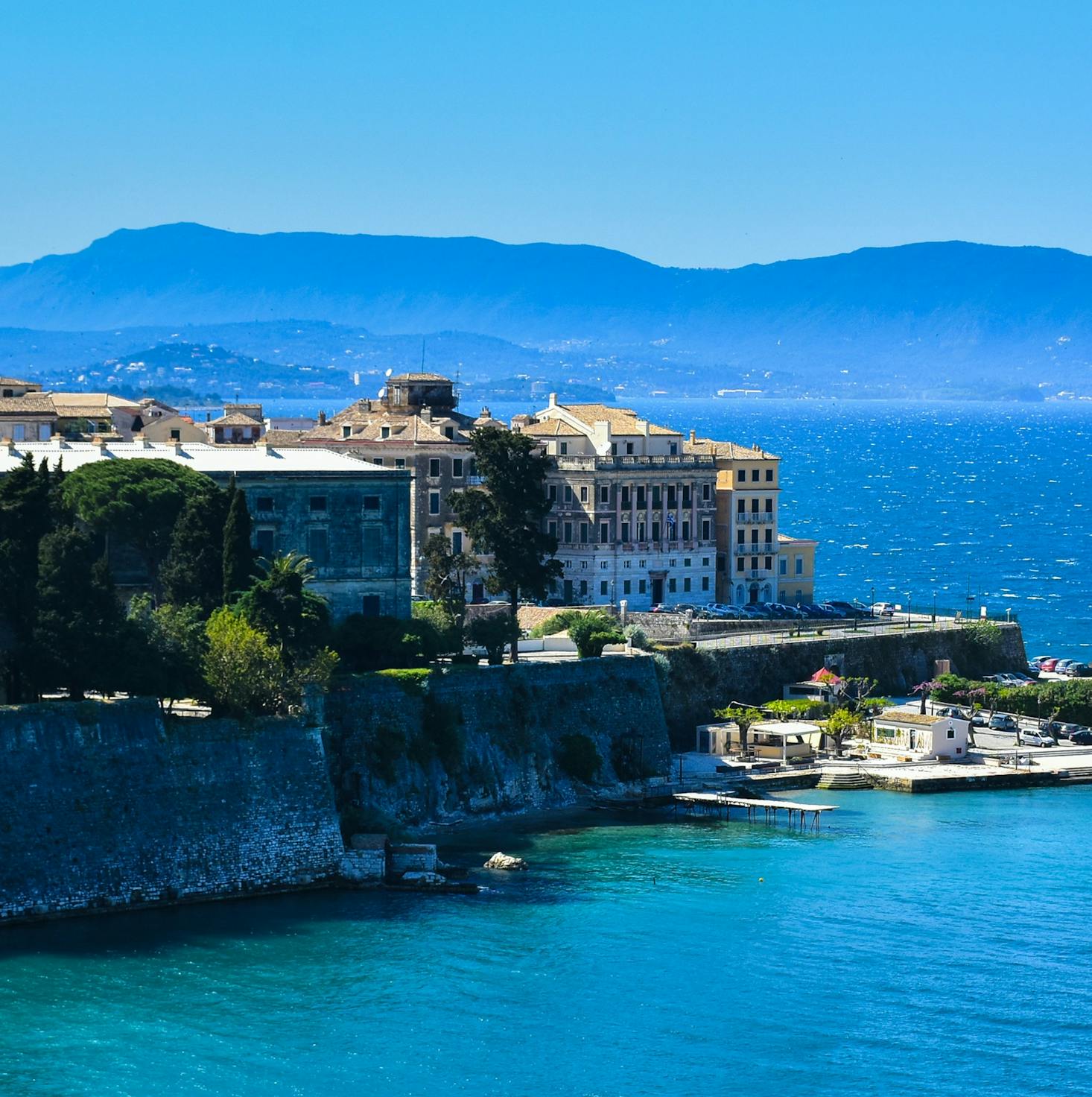 The city of Corfu overlooks the bright blue Ionian Sea under a sunny sky