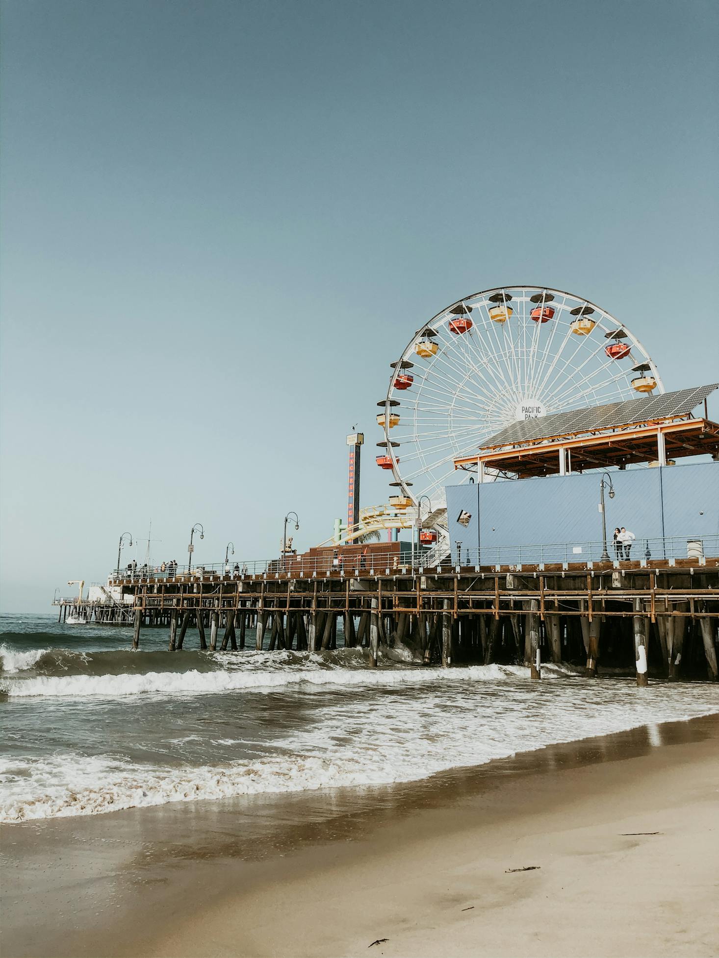 A view of the beach with crashing waves, Ferris wheel, and Santa Monica Pier