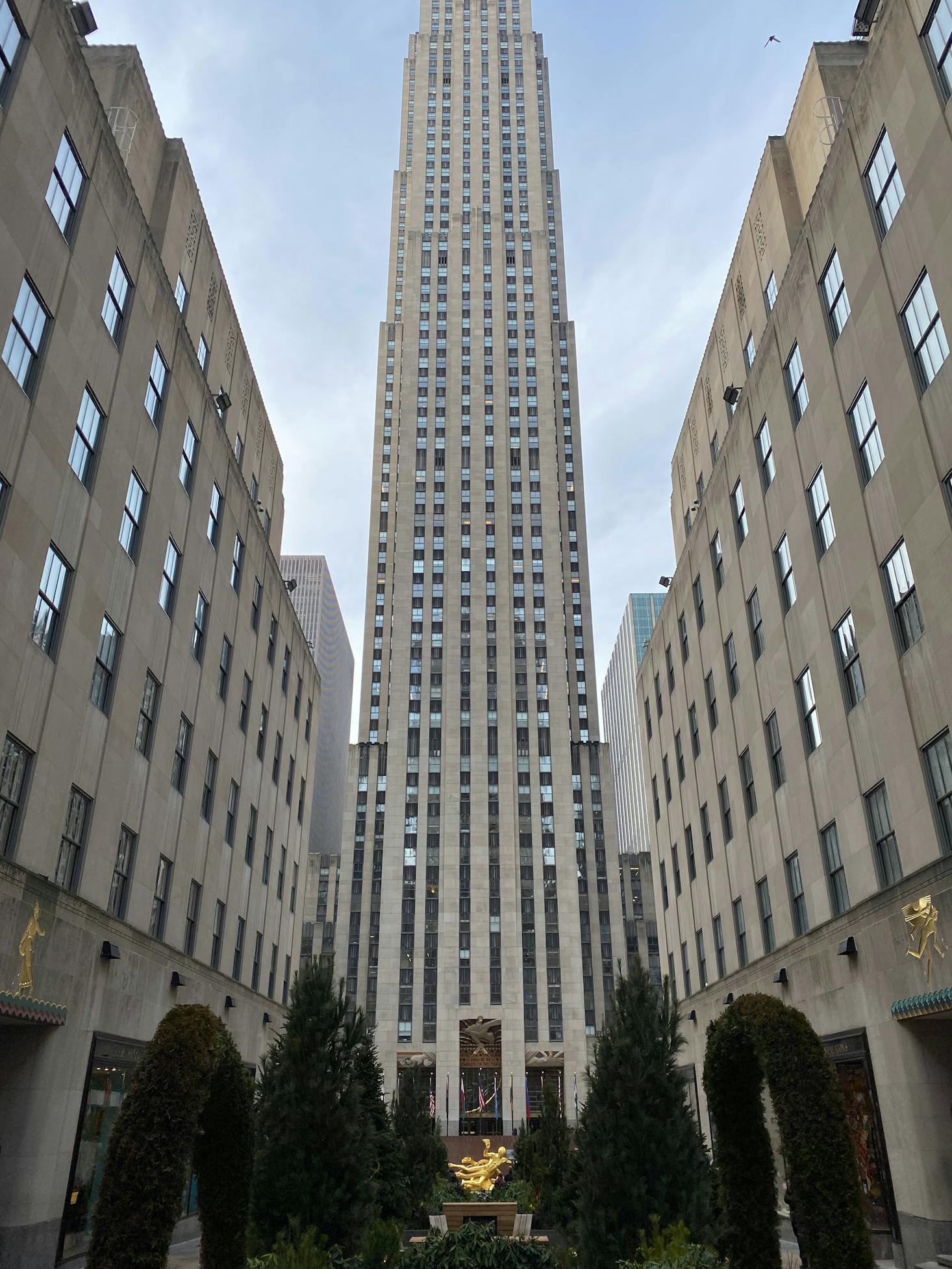 The tall grey building of Rockefeller Center in New York with other buildings surrounding it