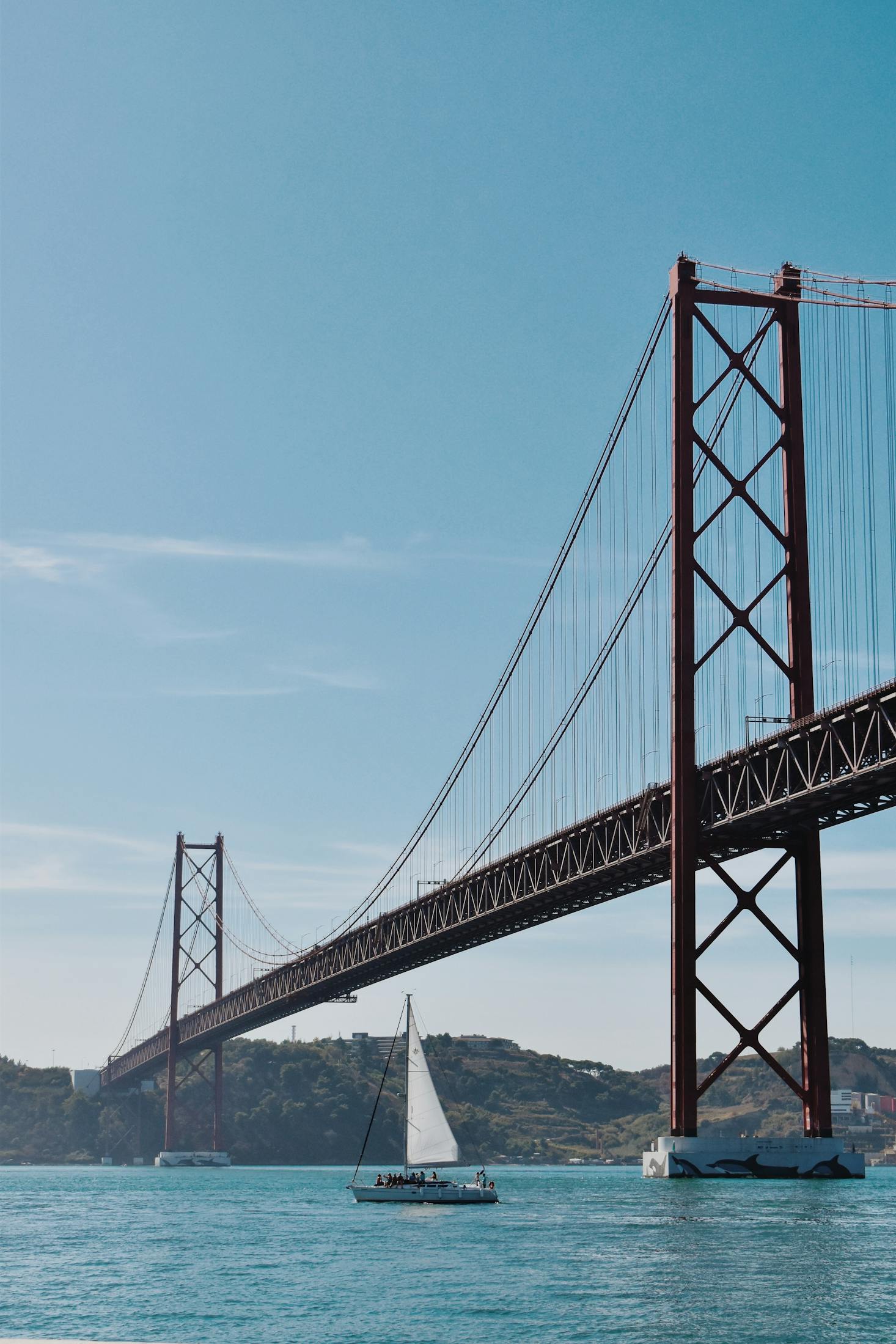 A sailboat sailing under a bridge in Lisbon with nearby luggage storage