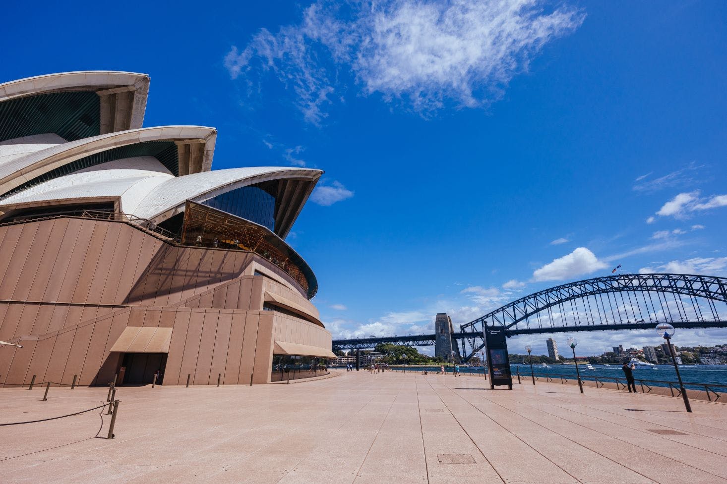 Sydney Opera House with golden hues and its matching promenade overlooking the waterfront and the Sydney Harbor Bridge