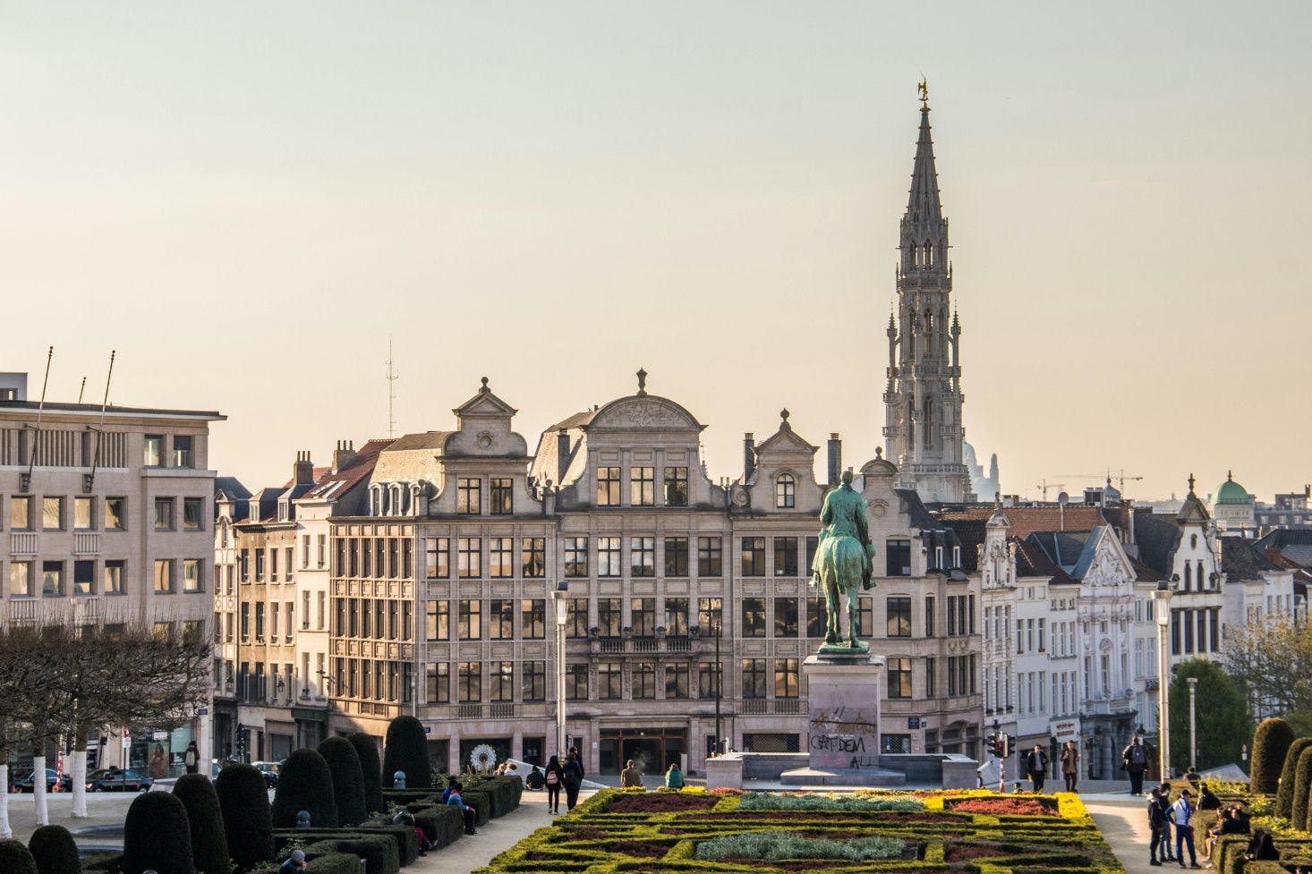 Mont des Arts monument in Brussels, with green hedges around and other buildings, and the spire of the Town Hall towering behind