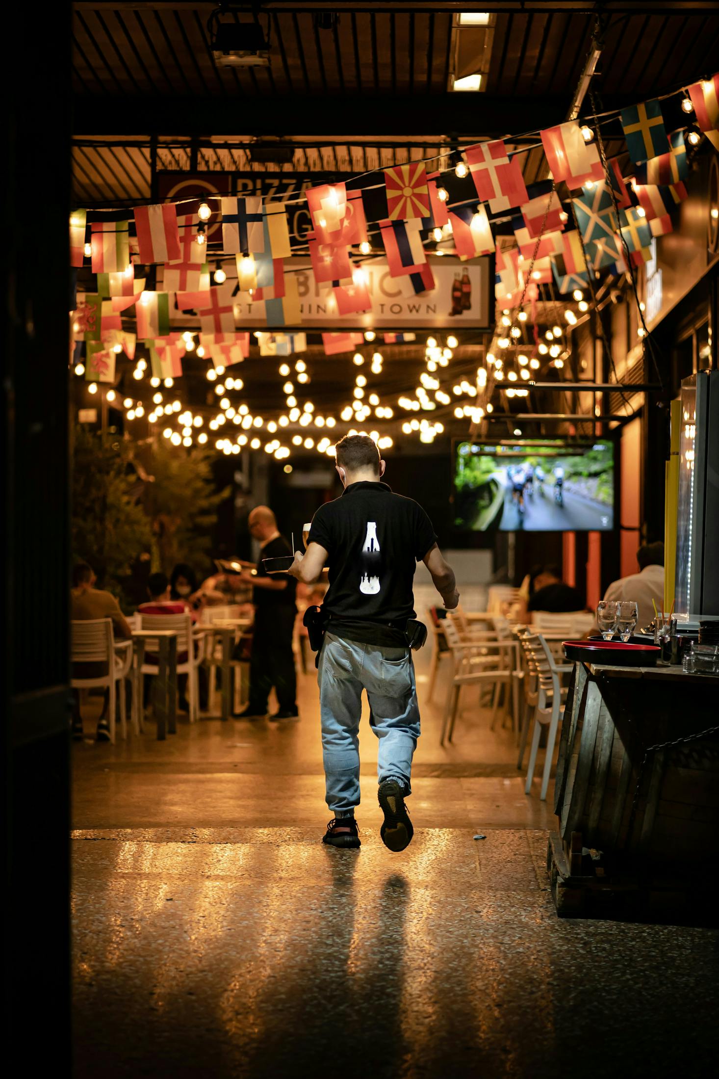 A server walking to a bunch of outdoor tables lit with twinkle lights in Bologna at night