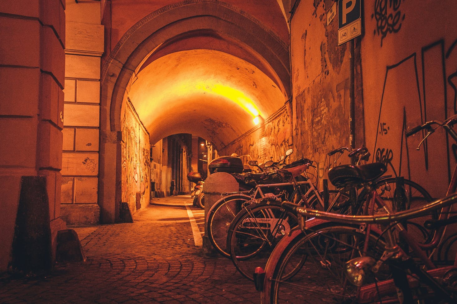 An alleyway at night in Bologna with orange light and parked bicycles