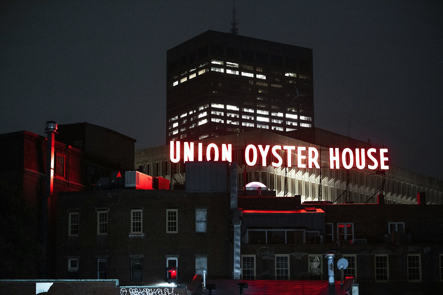 A large, white neon "Union Oyster House" sign among the buildings in Boston at night