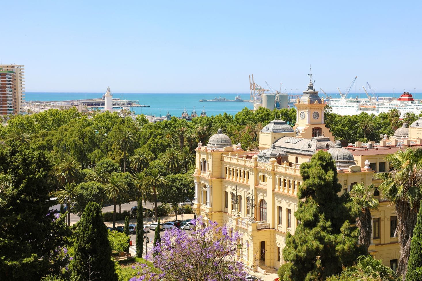 Málaga Cathedral surrounded by lush trees, with the port and sea in the background