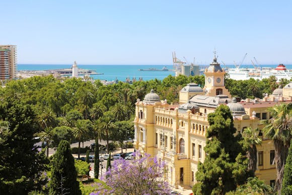 Málaga Cathedral surrounded by lush trees, with the port and sea in the background